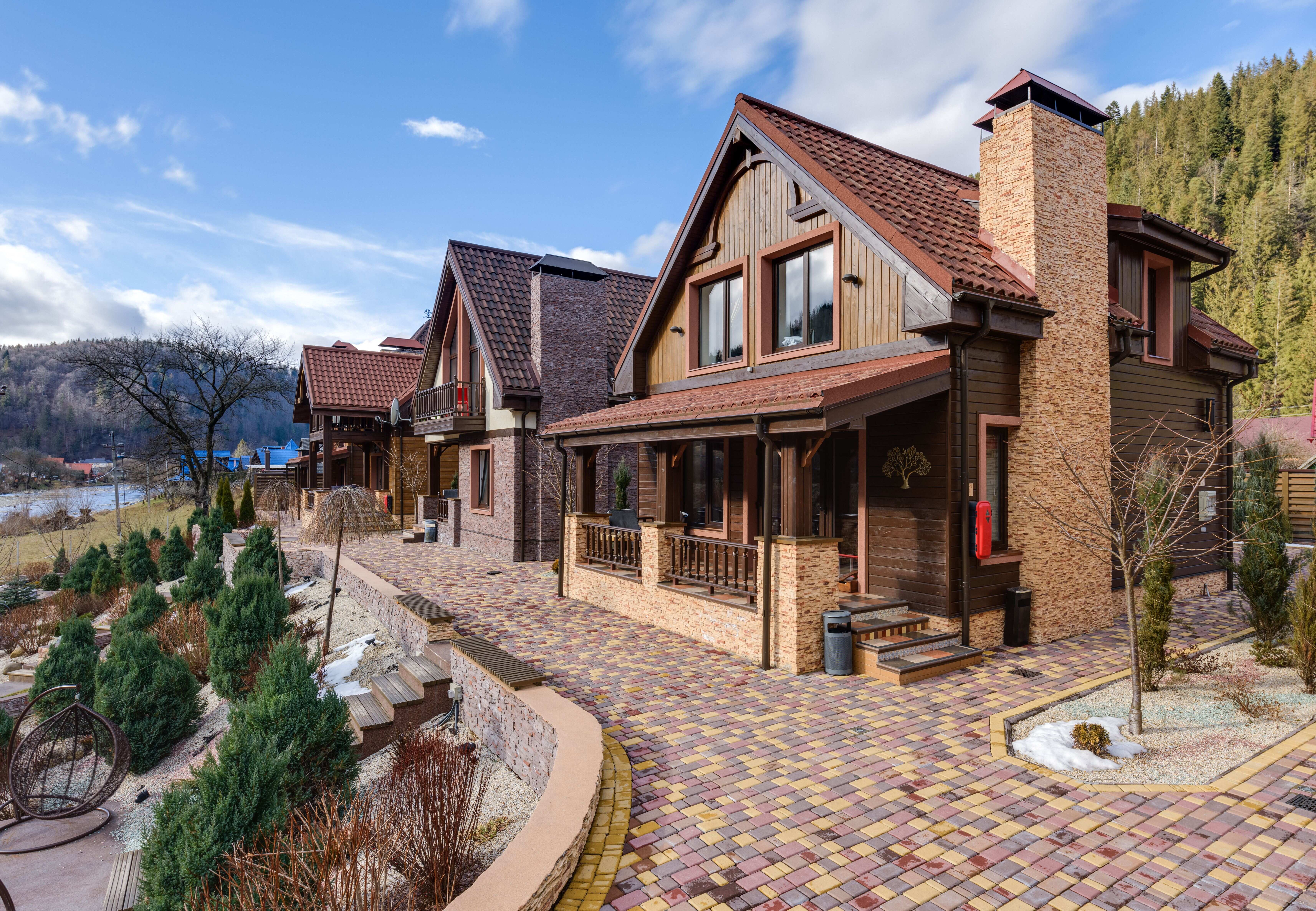 A paved walkway lined with modern wooden resort chalets set against a forest mountain backdrop.