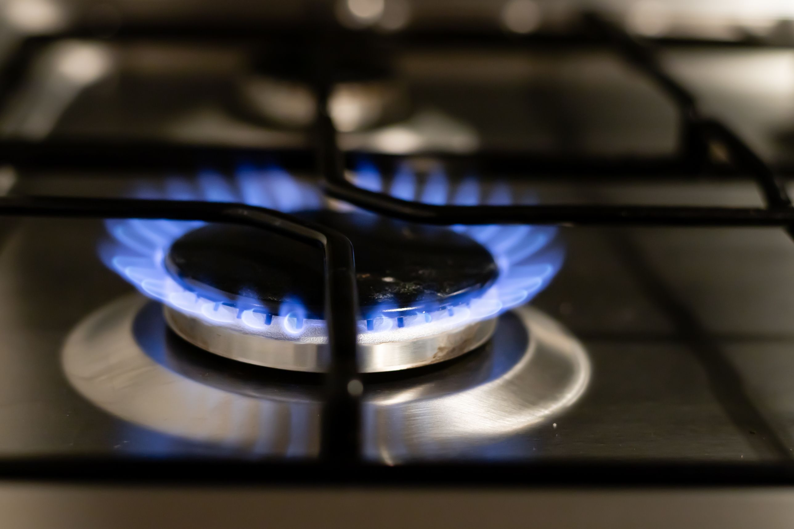 A close-up view of a blue gas flame burning steadily on a stainless steel stove burner.