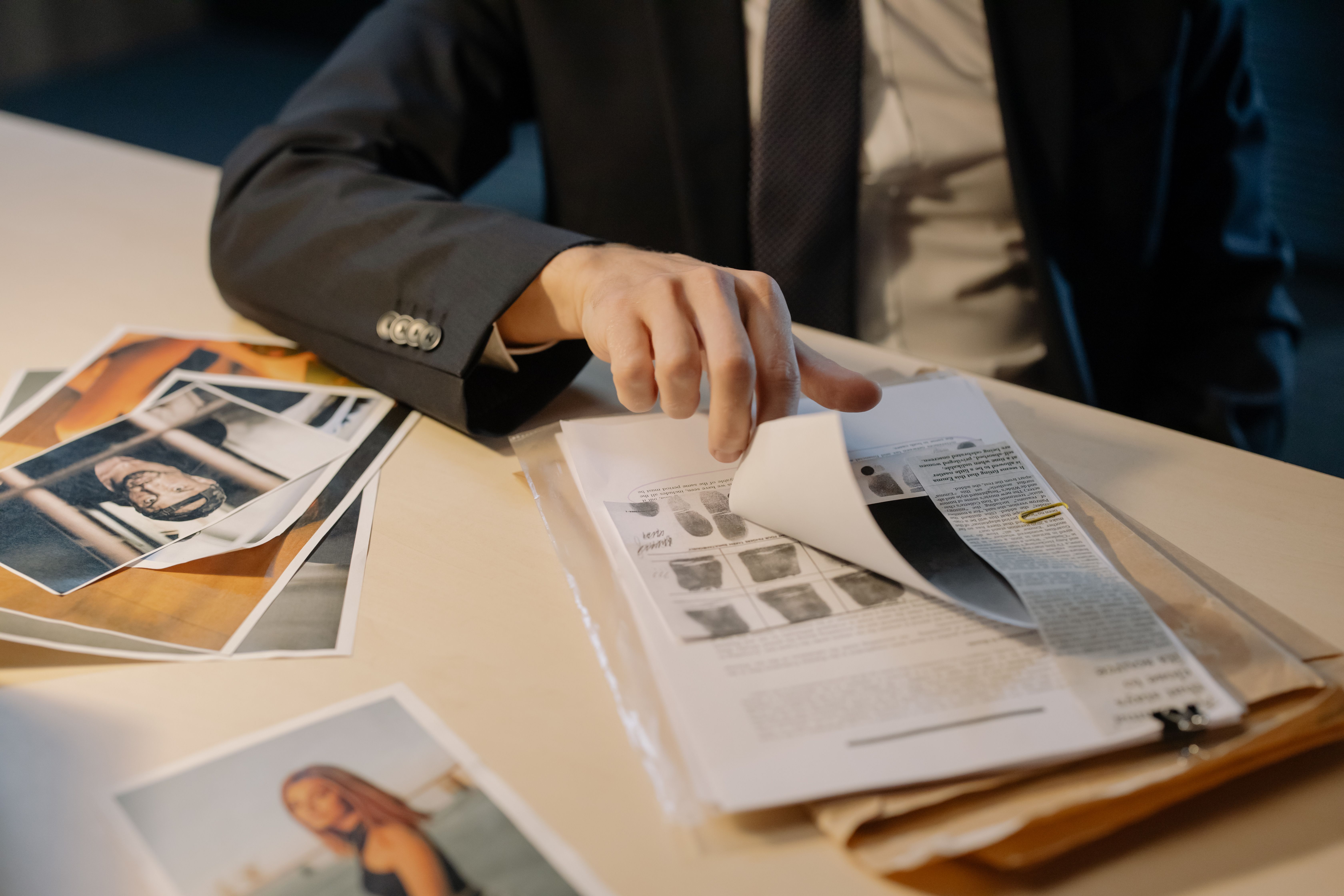 A person in a business suit flipping through document pages alongside printed photos on a desk.