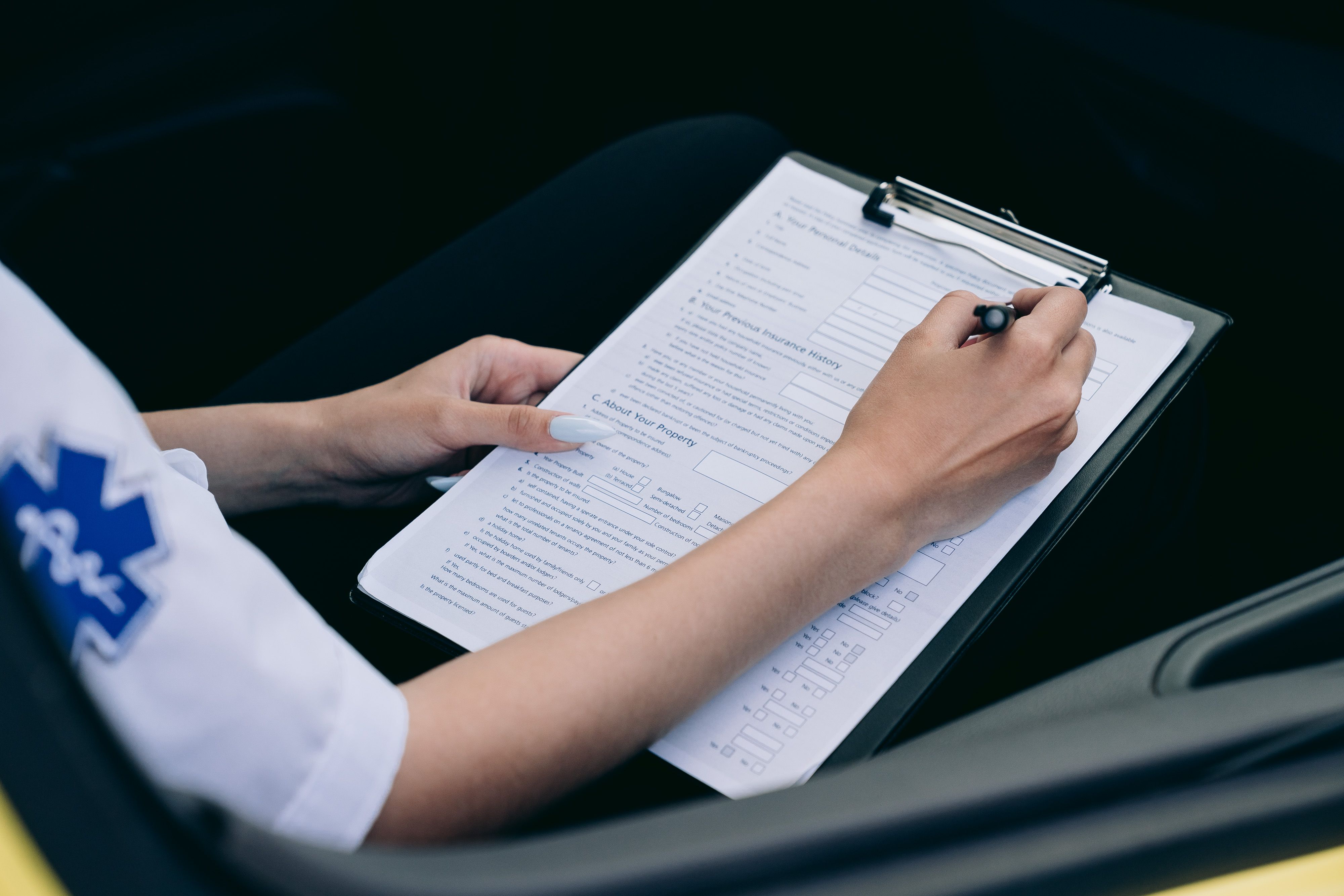 A paramedic filling out an official medical report form attached to a clipboard inside a vehicle.
