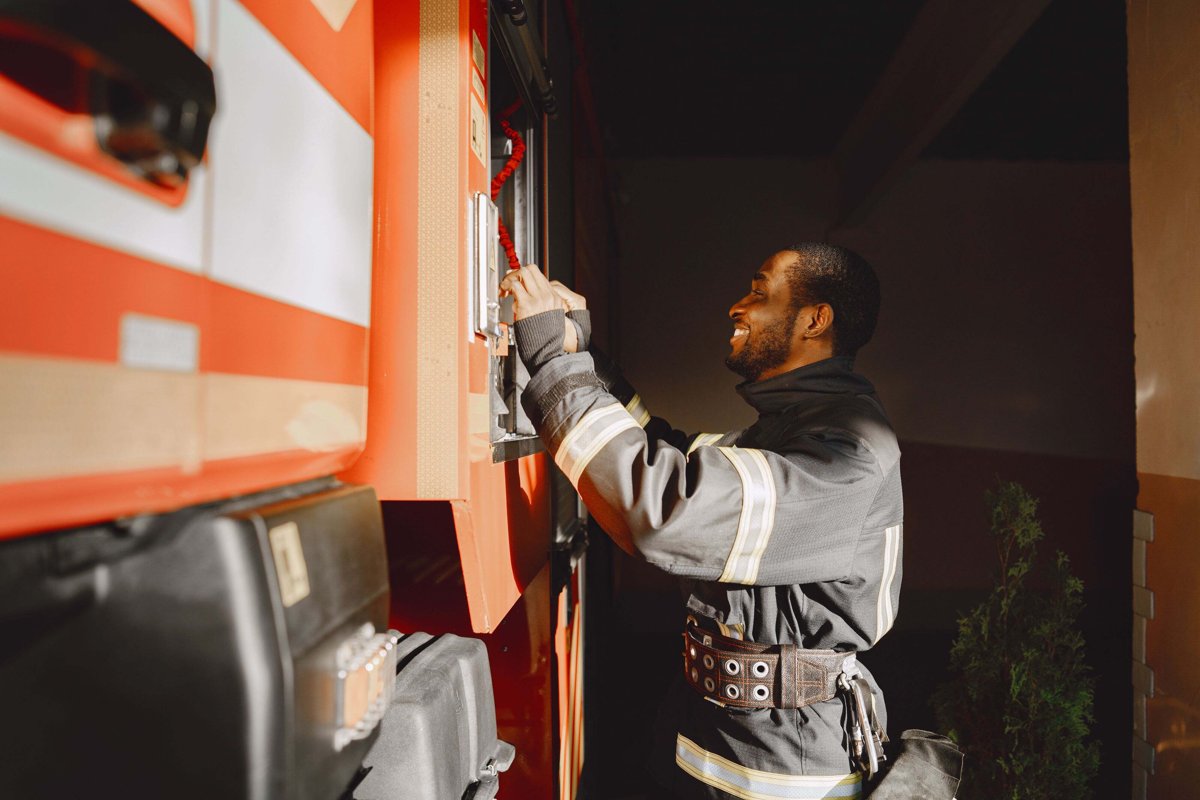 A firefighter in protective gear operating equipment on the side of a red fire truck.