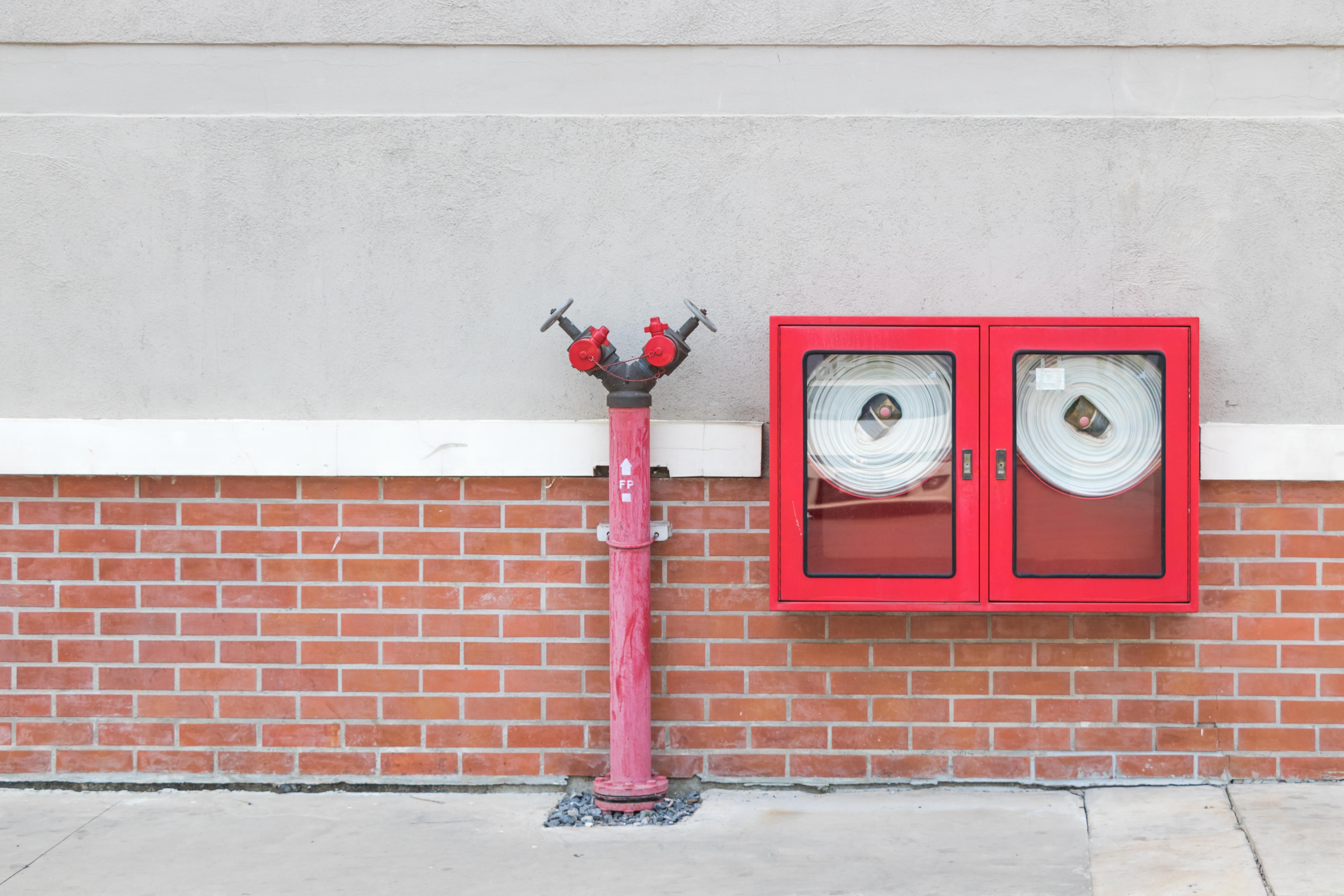 A red standpipe inlet and a wall-mounted red cabinet containing coiled fire hoses mounted against a brick wall.