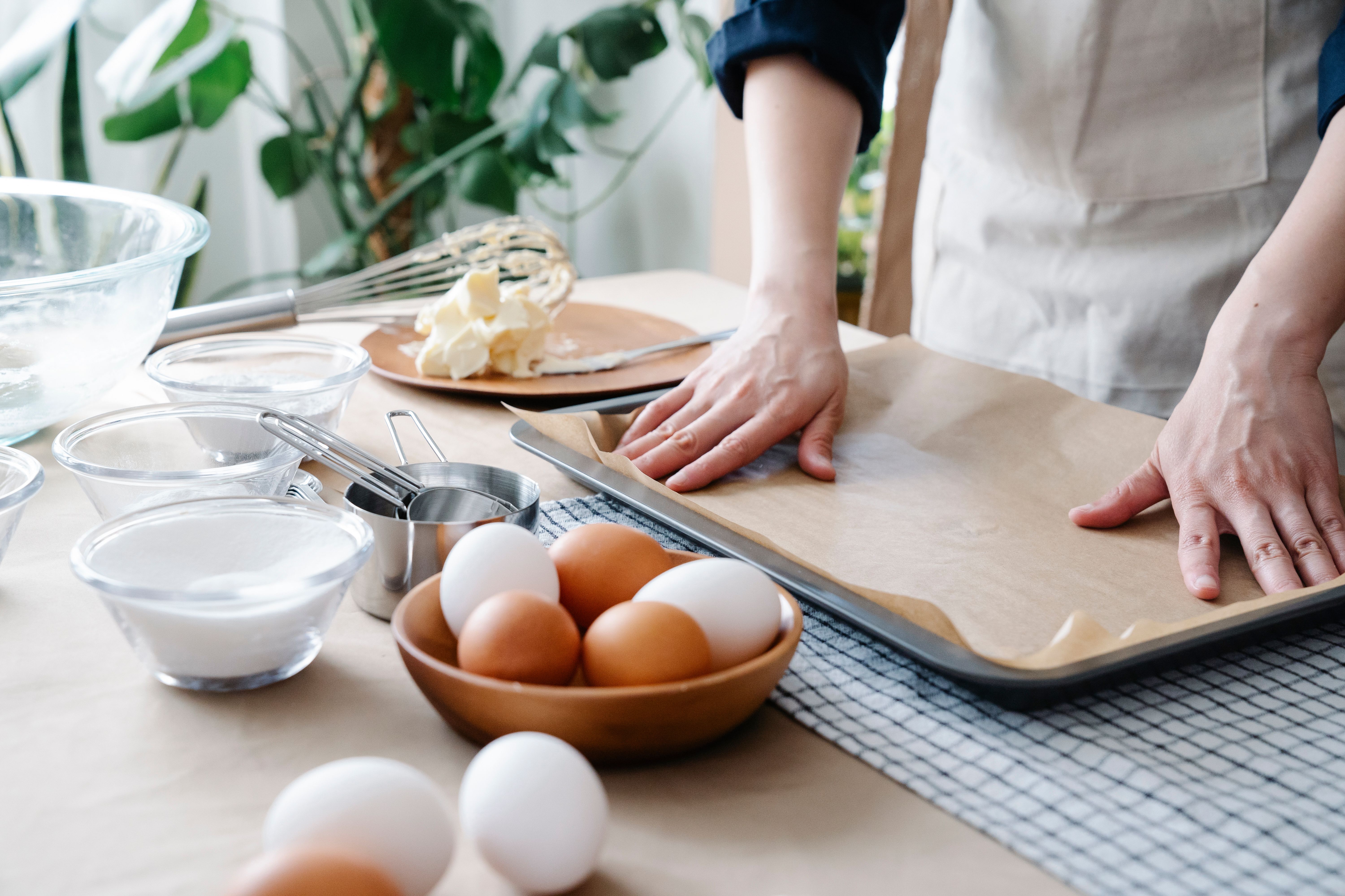 A baker lining a metal baking sheet with parchment paper surrounded by baking ingredients like eggs, sugar, and butter. Label safety potions.jpg