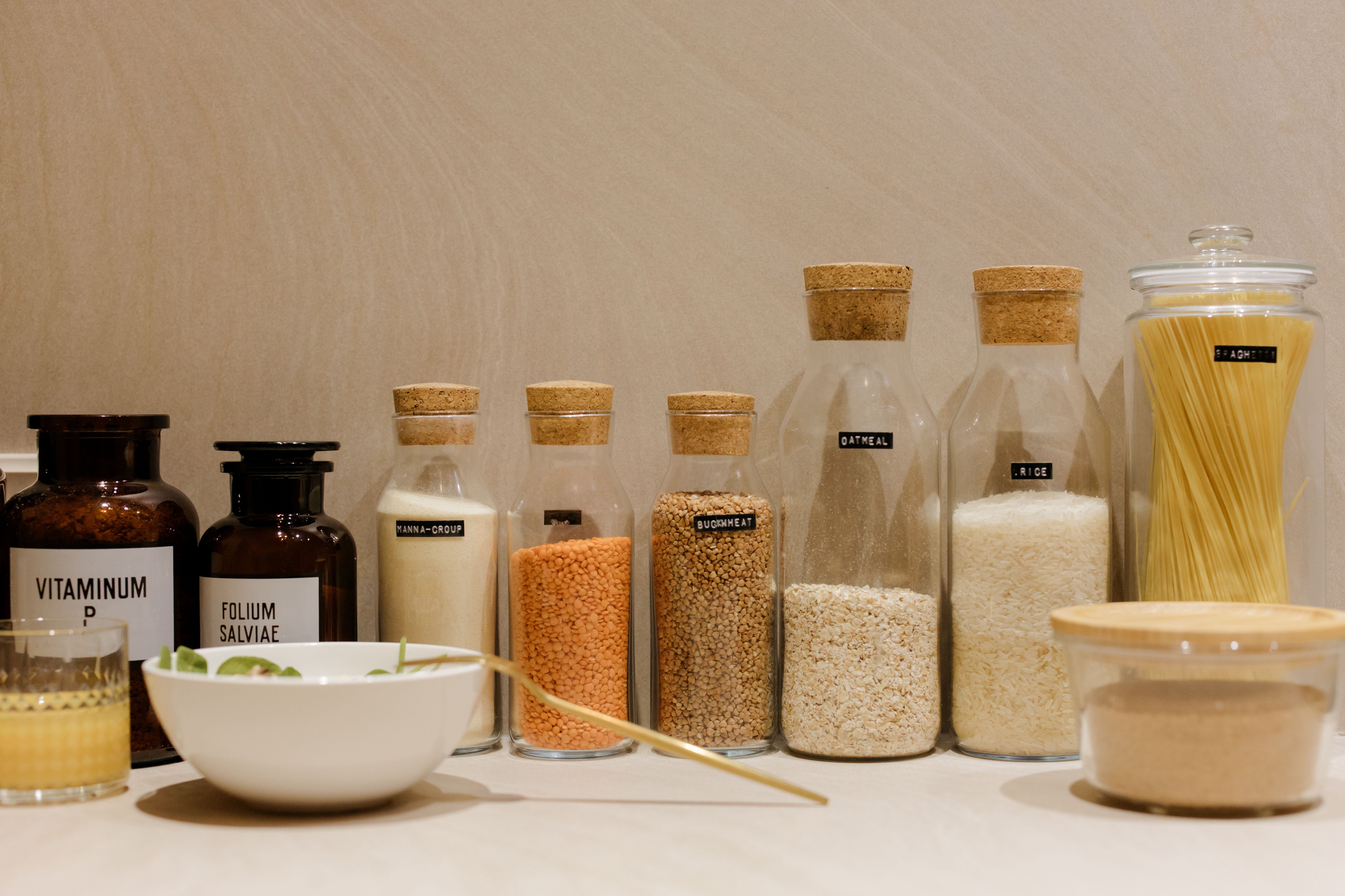 A lineup of labeled glass storage jars filled with pantry staples like rice, oatmeal, lentils, and pasta on a counter.