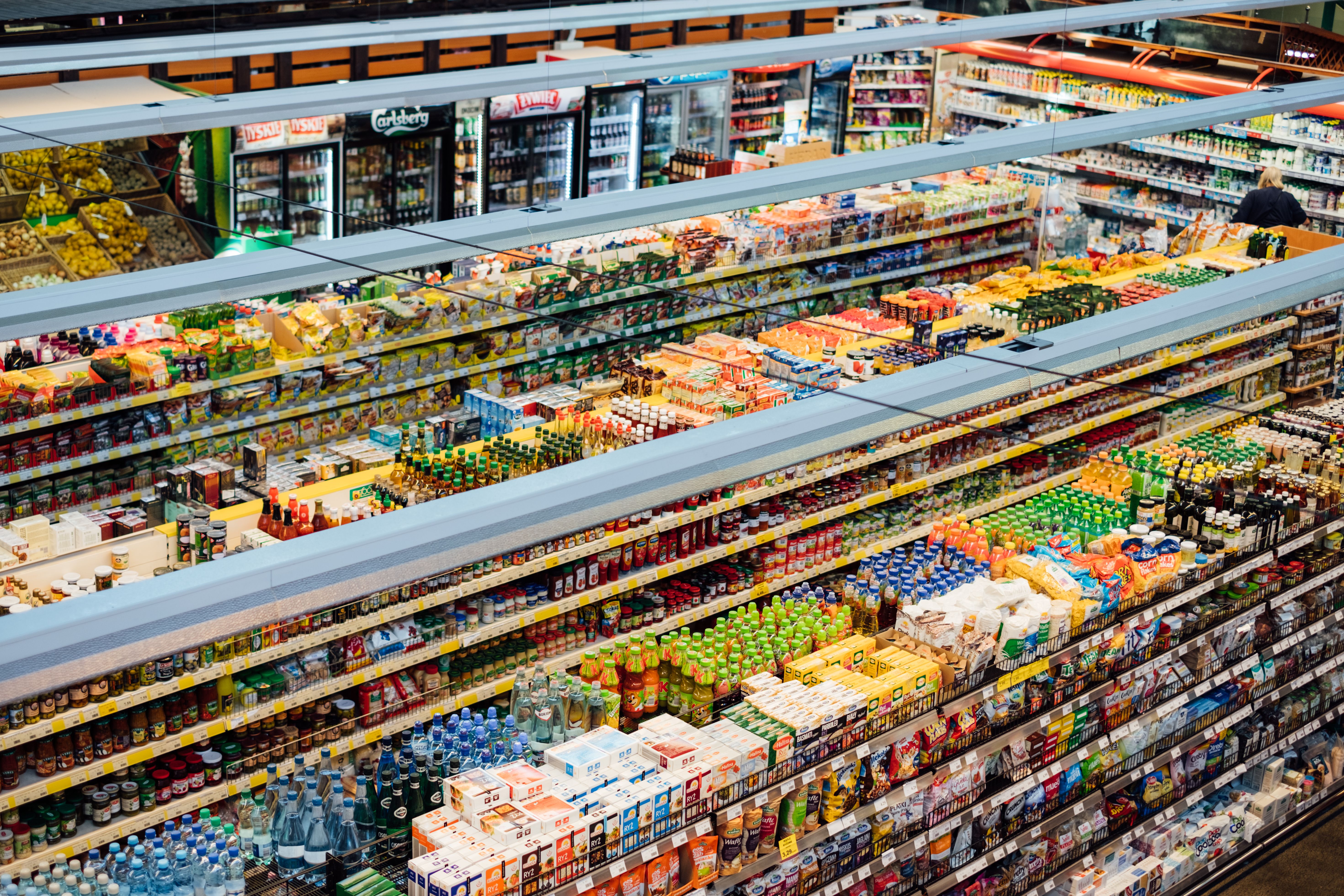 High-angle, overhead view of fully stocked grocery store aisles filled with colorful packaged food products and drinks.