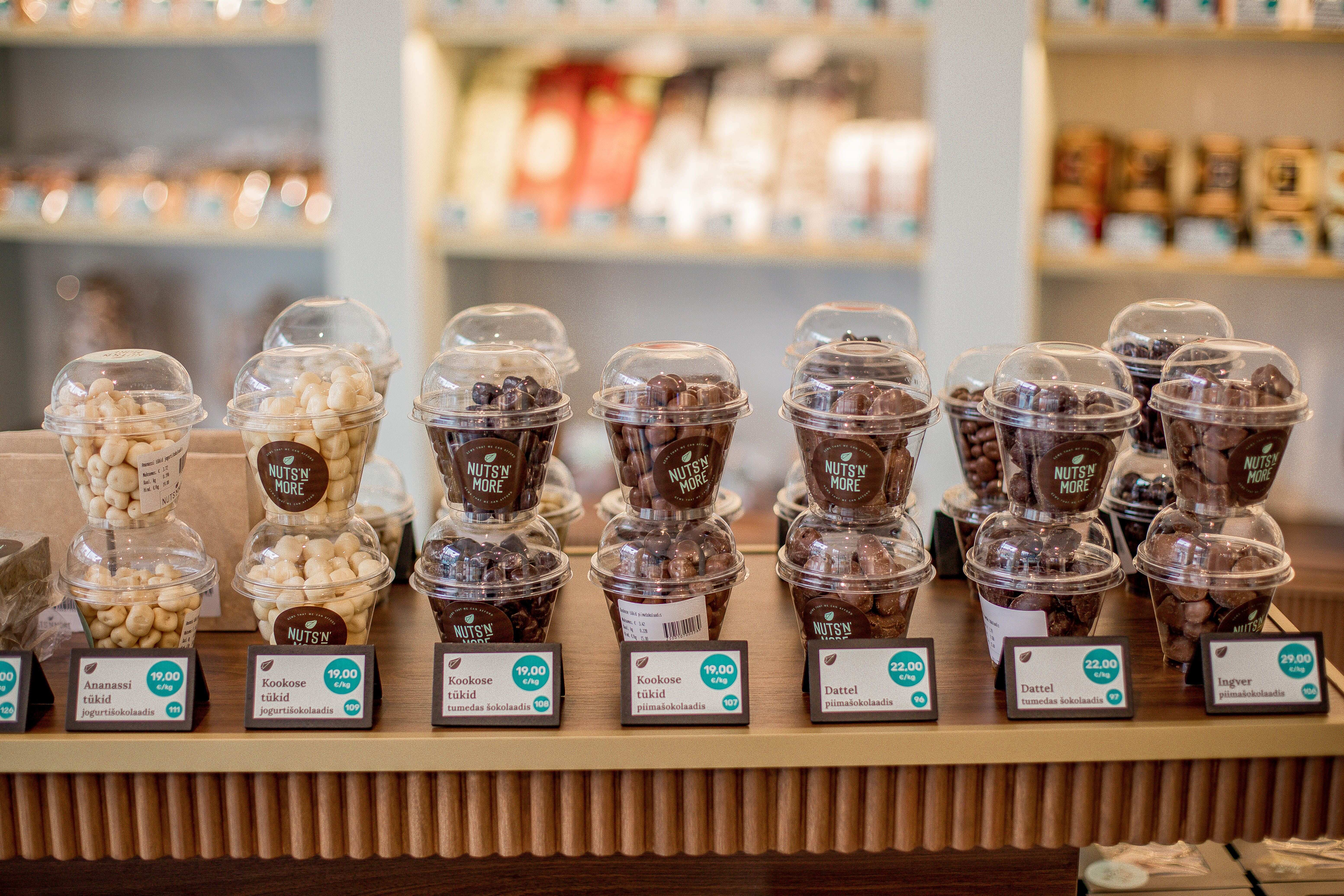 Plastic cups filled with assorted chocolate-covered nuts and dried fruits displayed with price tags on a store counter.