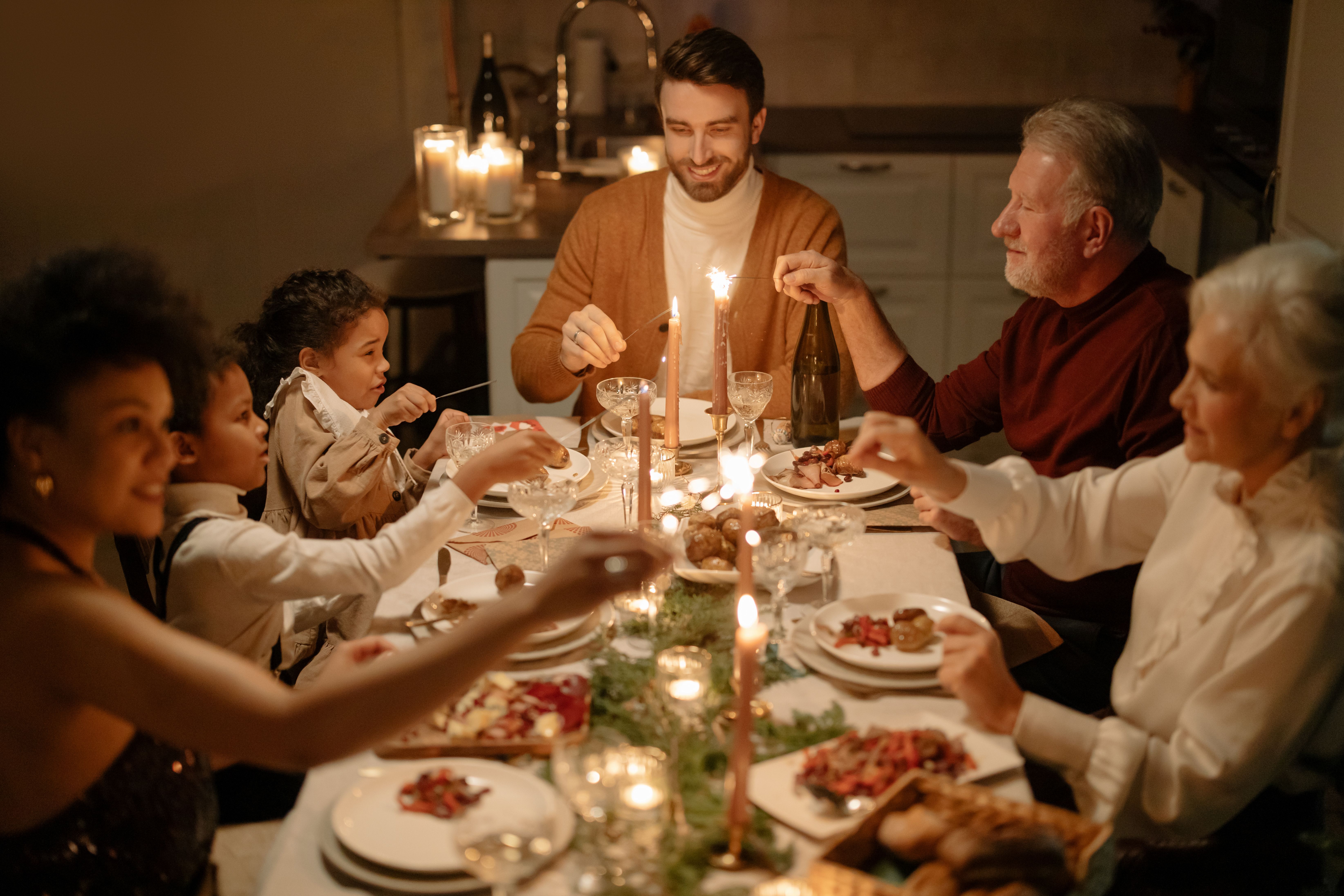 A family gathering around a candlelit holiday dinner table holding sparklers and enjoying a festive meal together.