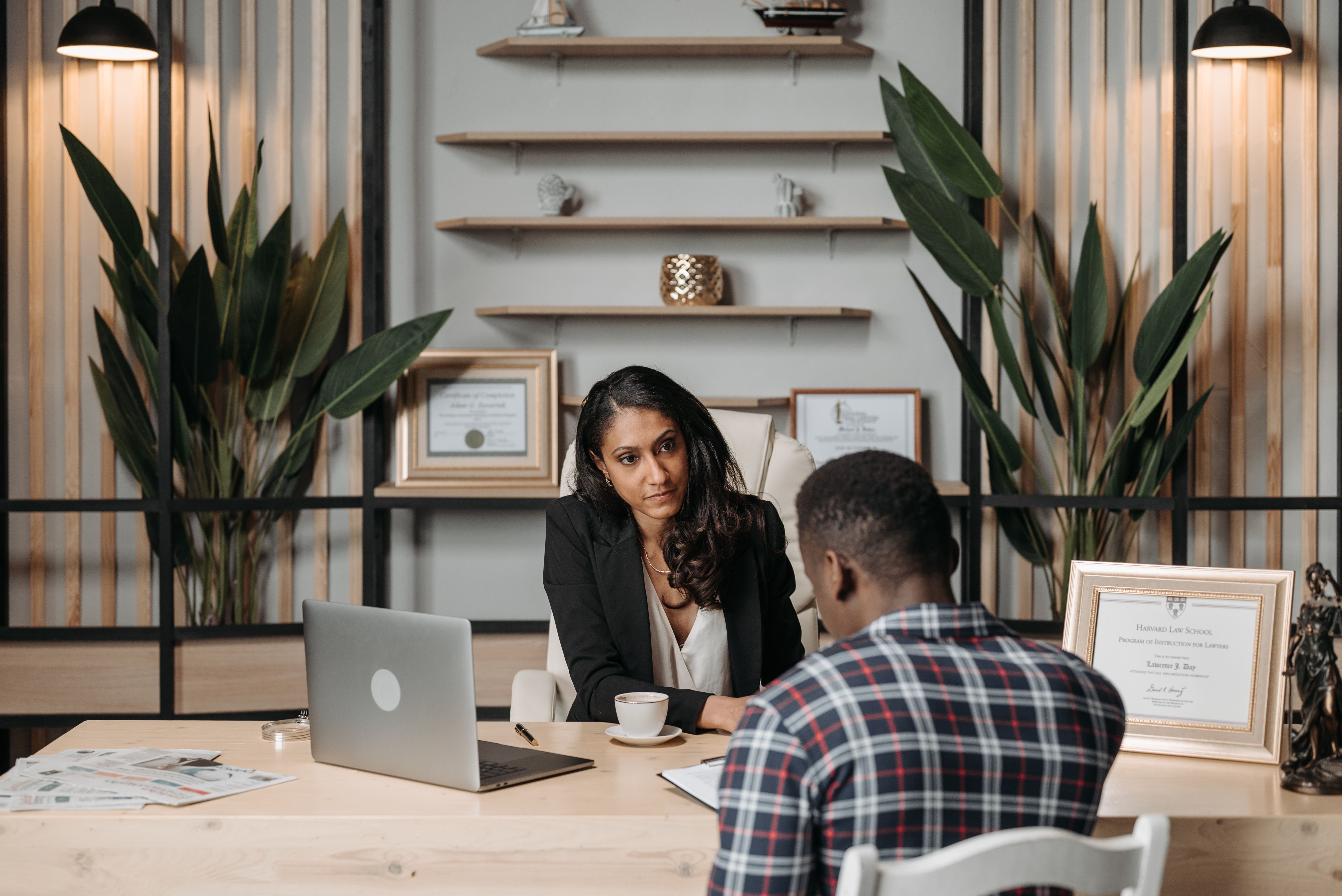 A professional woman in a dark blazer consulting with a client across a wooden desk in a modern office.