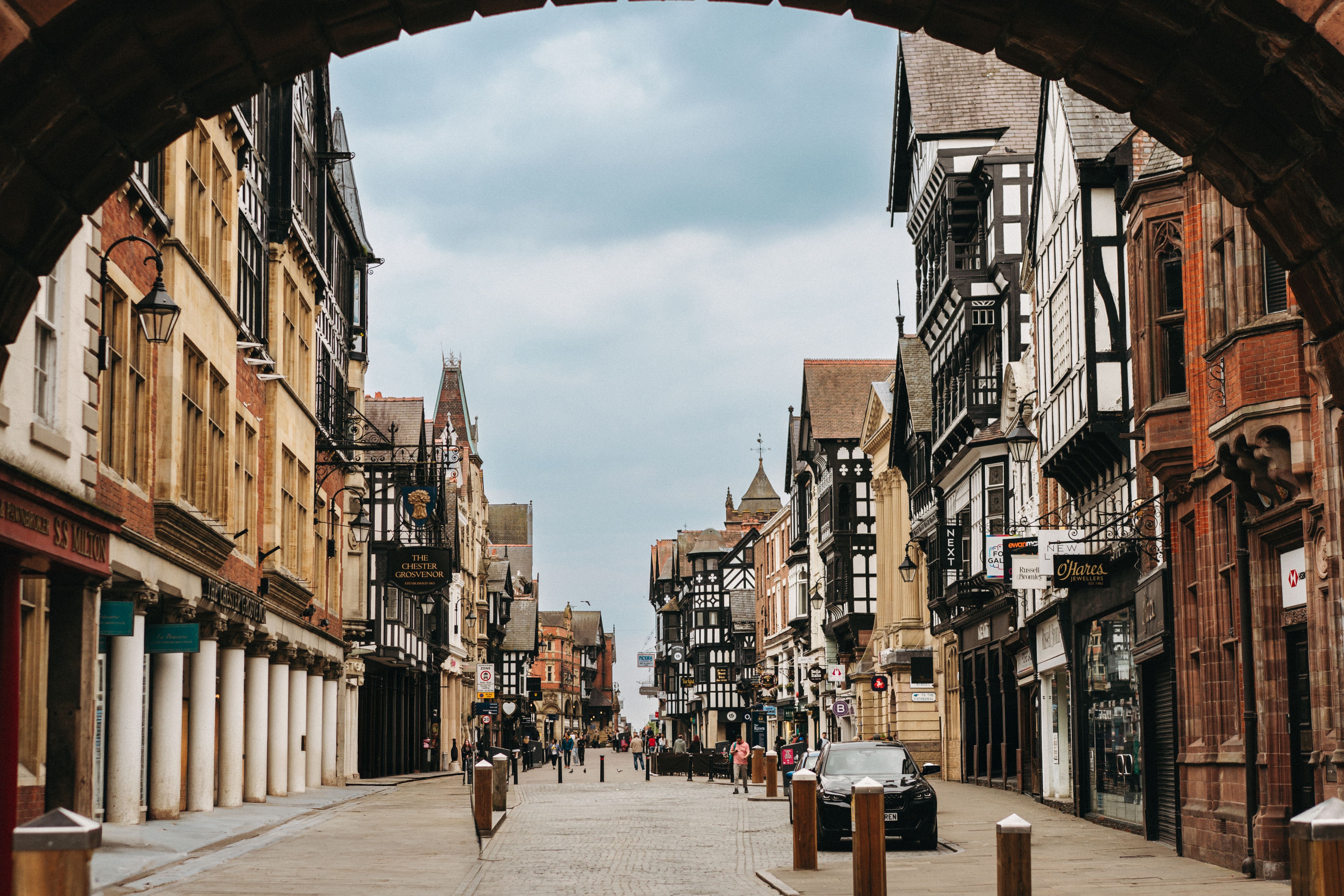 View through an archway looking down a historic cobblestone street lined with traditional timber-framed buildings and shops.