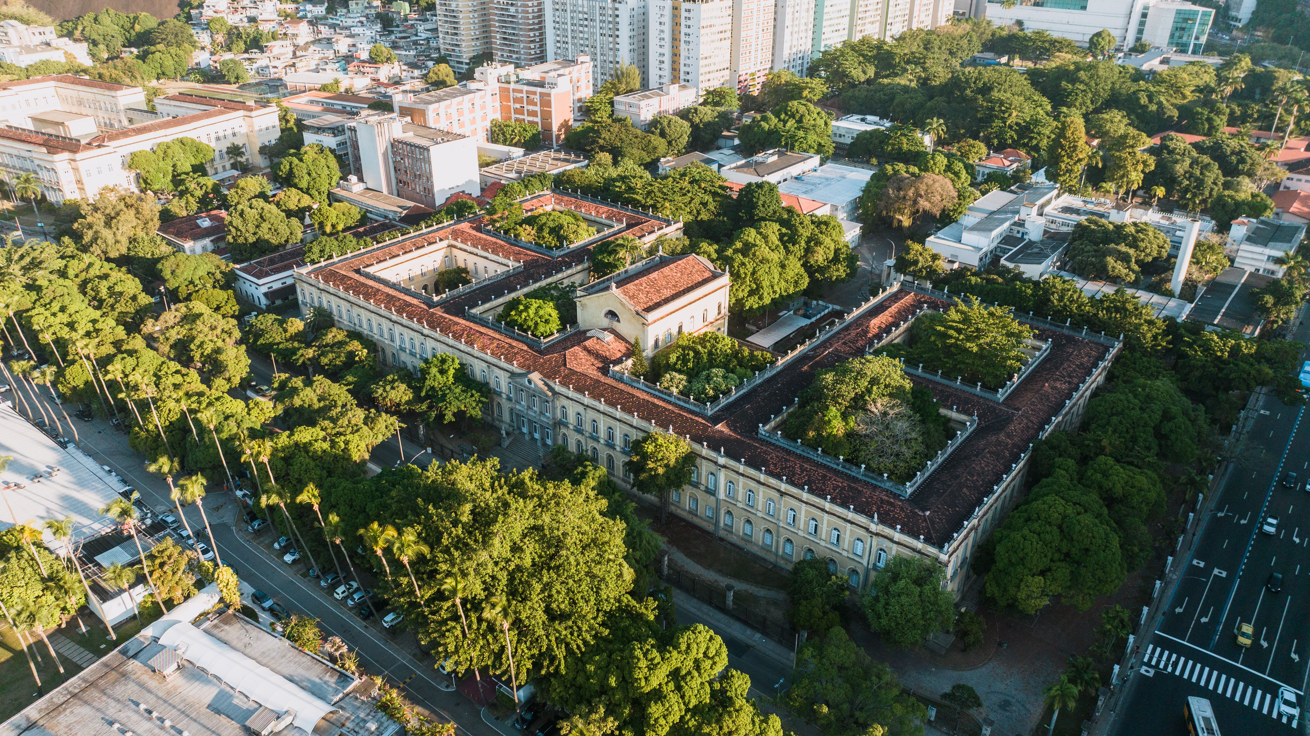 High-angle aerial view of a large historic school campus with tile-roofed buildings surrounded by trees and urban streets.