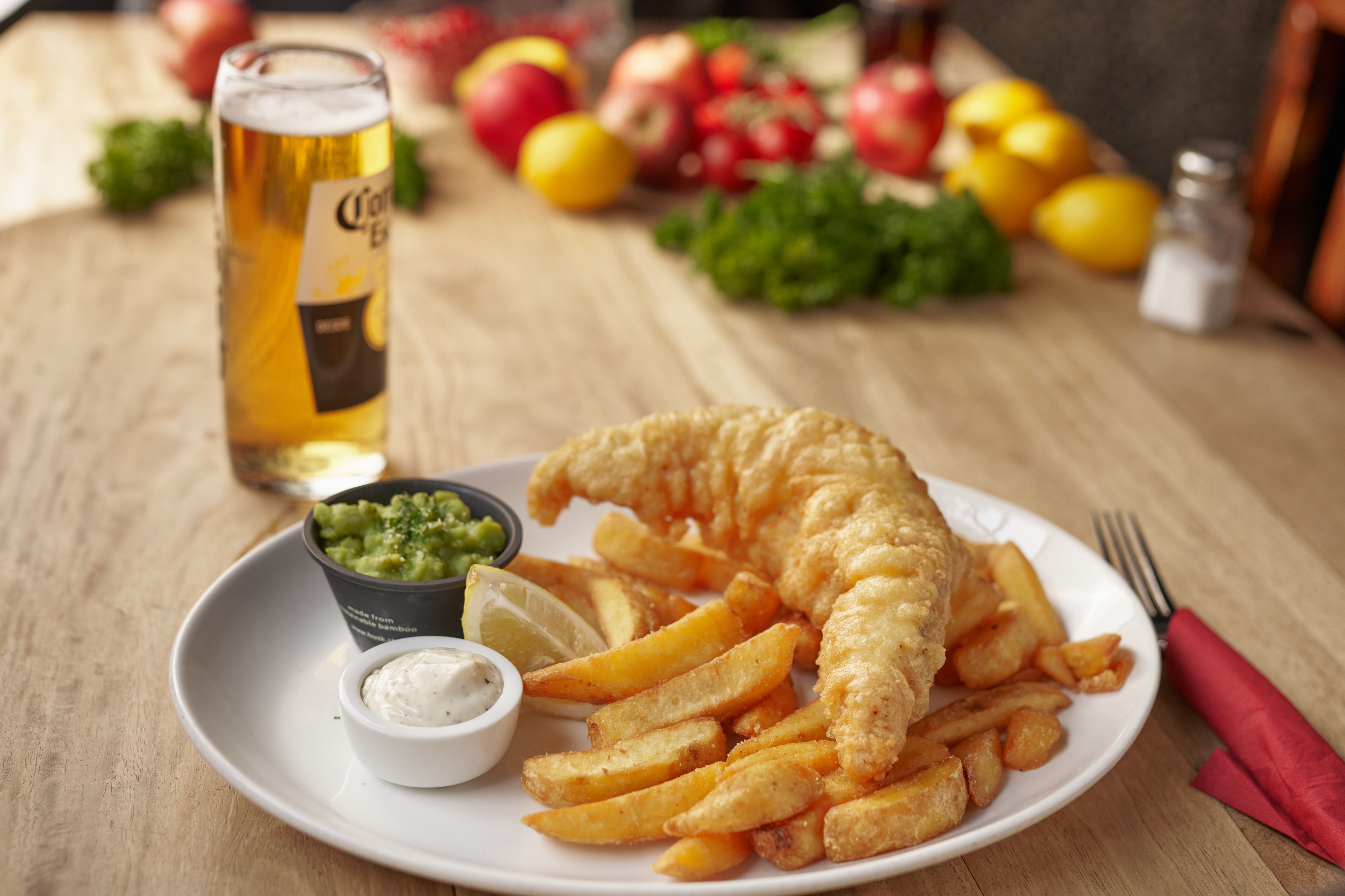 Plate of beer-battered fish and chips served with lemon, tartar sauce, mushy peas, and a glass of beer.