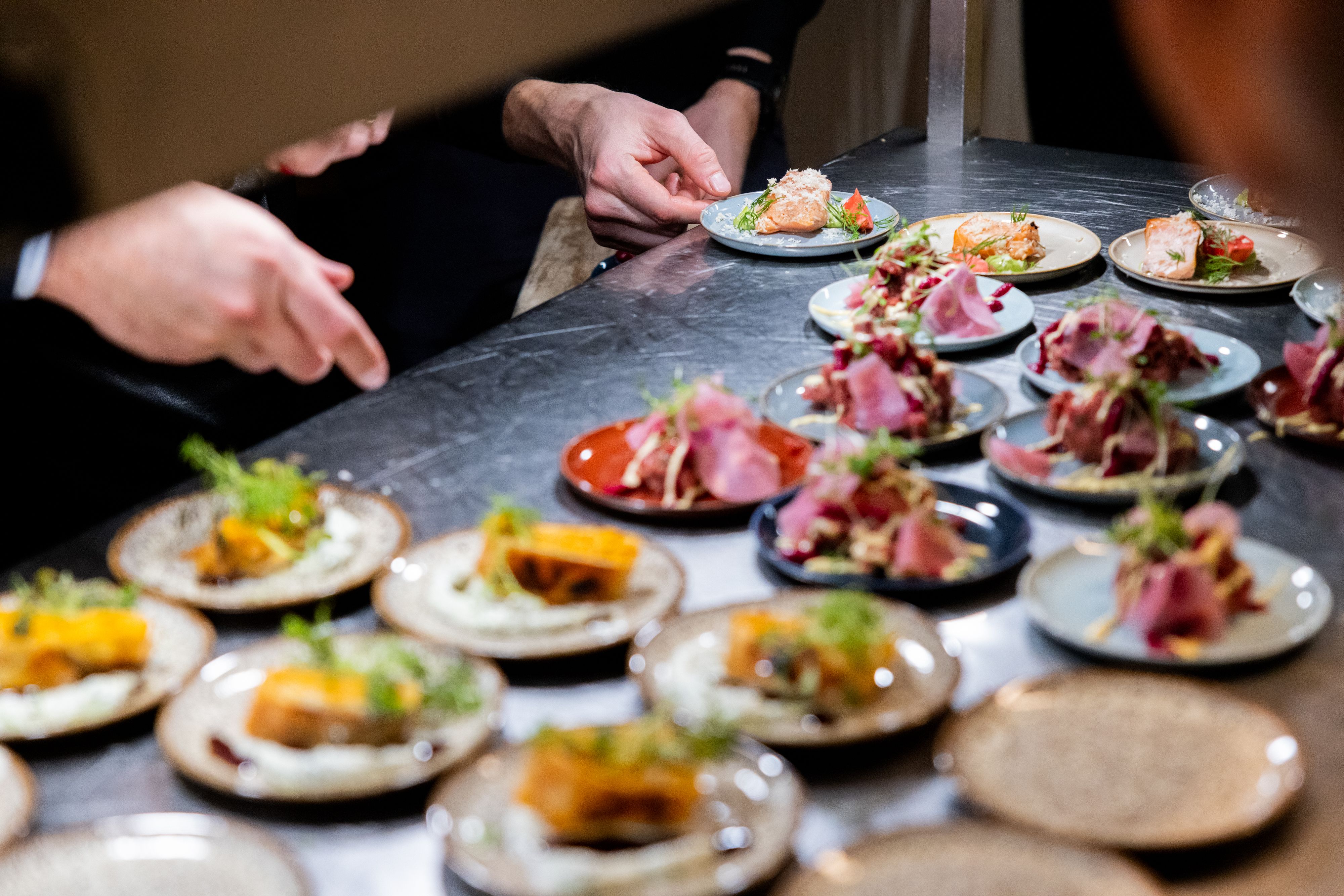 Hands of kitchen staff arranging and plating gourmet appetizers on a pass counter.