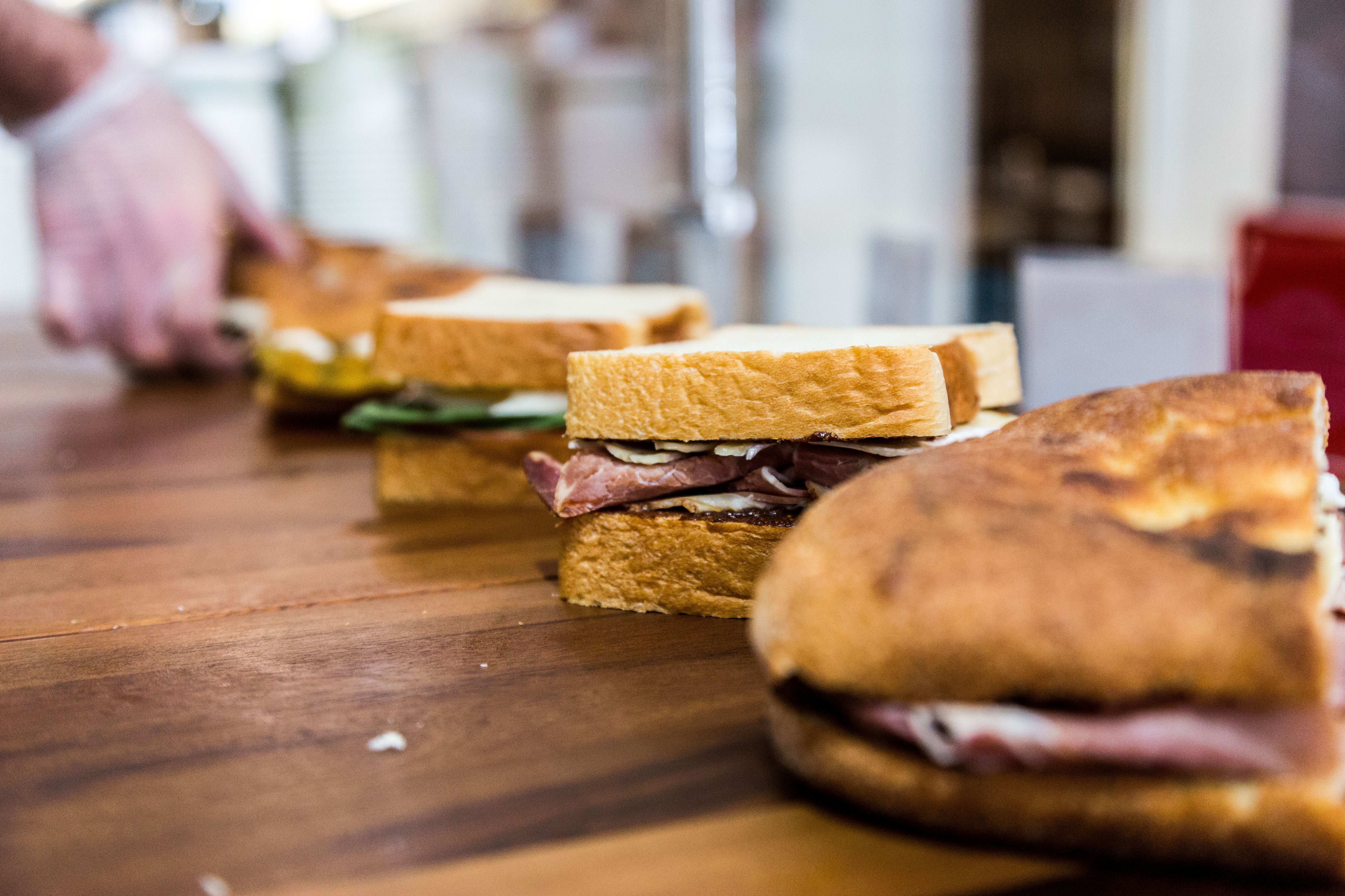 Row of freshly prepared sandwiches lined up on a wooden counter in a commercial prep area.