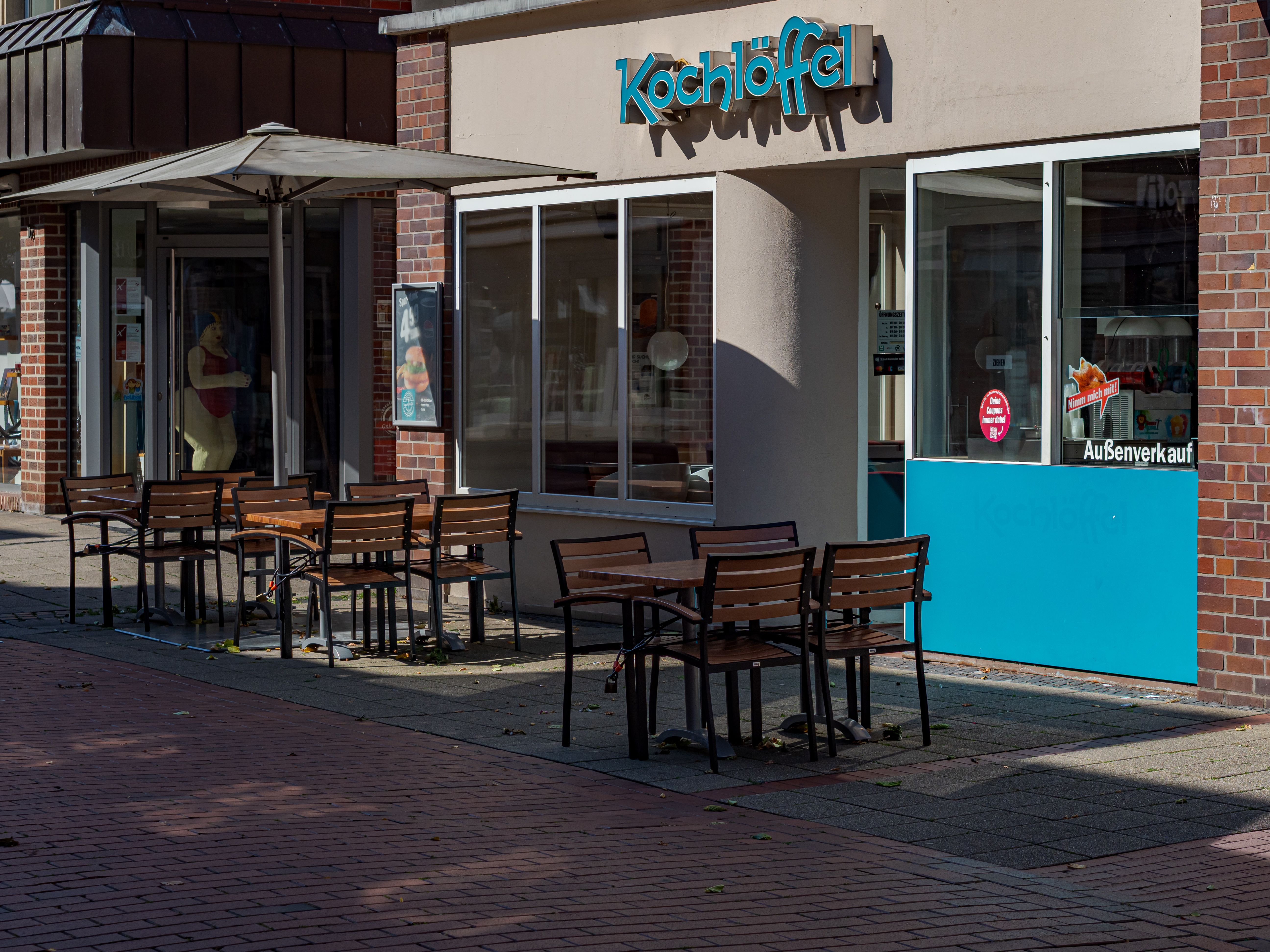 Exterior view of a fast-food restaurant storefront named Kochlöffel featuring outdoor patio seating with wooden tables and chairs.