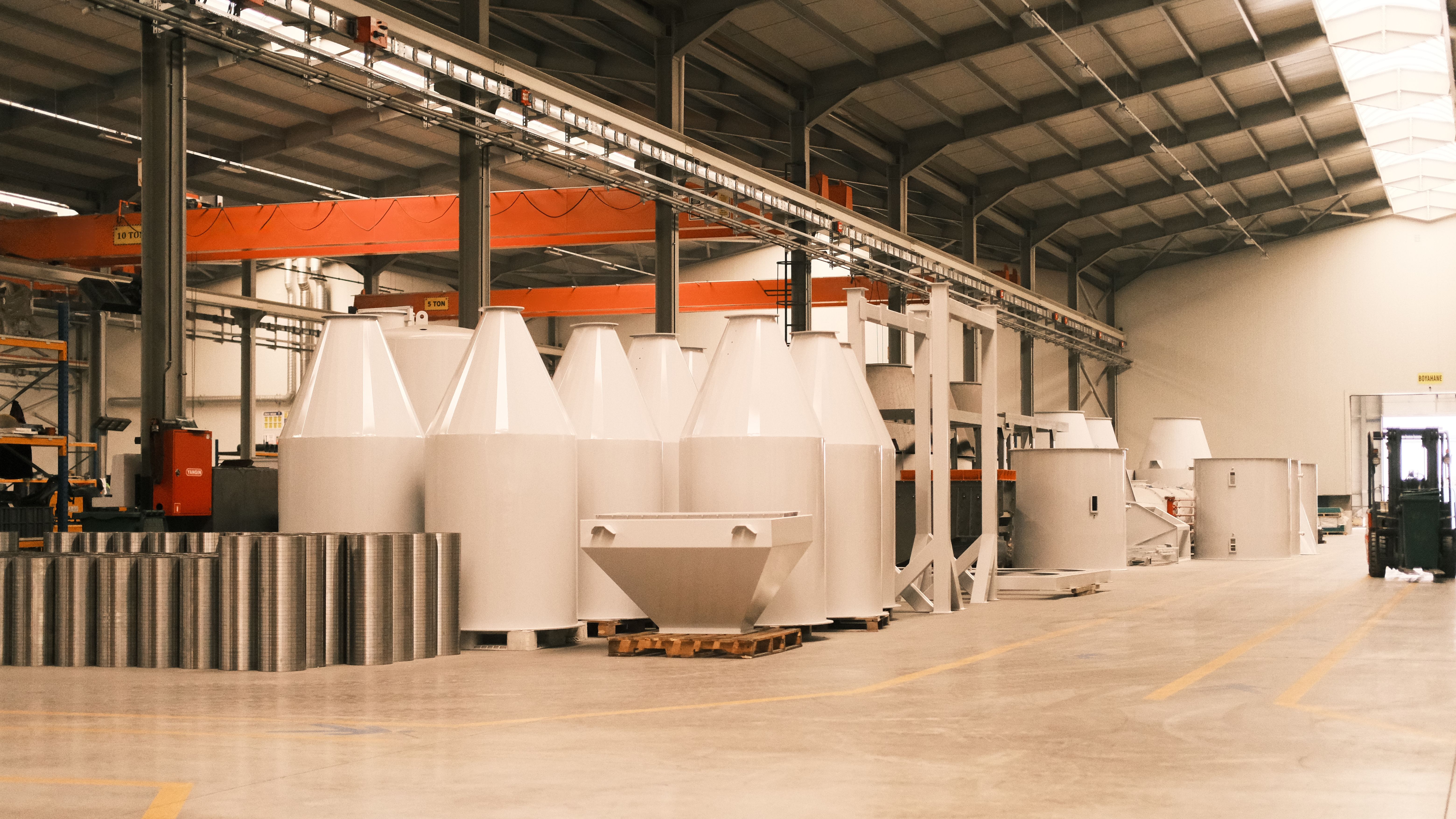 Spacious interior of an industrial manufacturing warehouse lined with large white processing tanks and metal equipment.