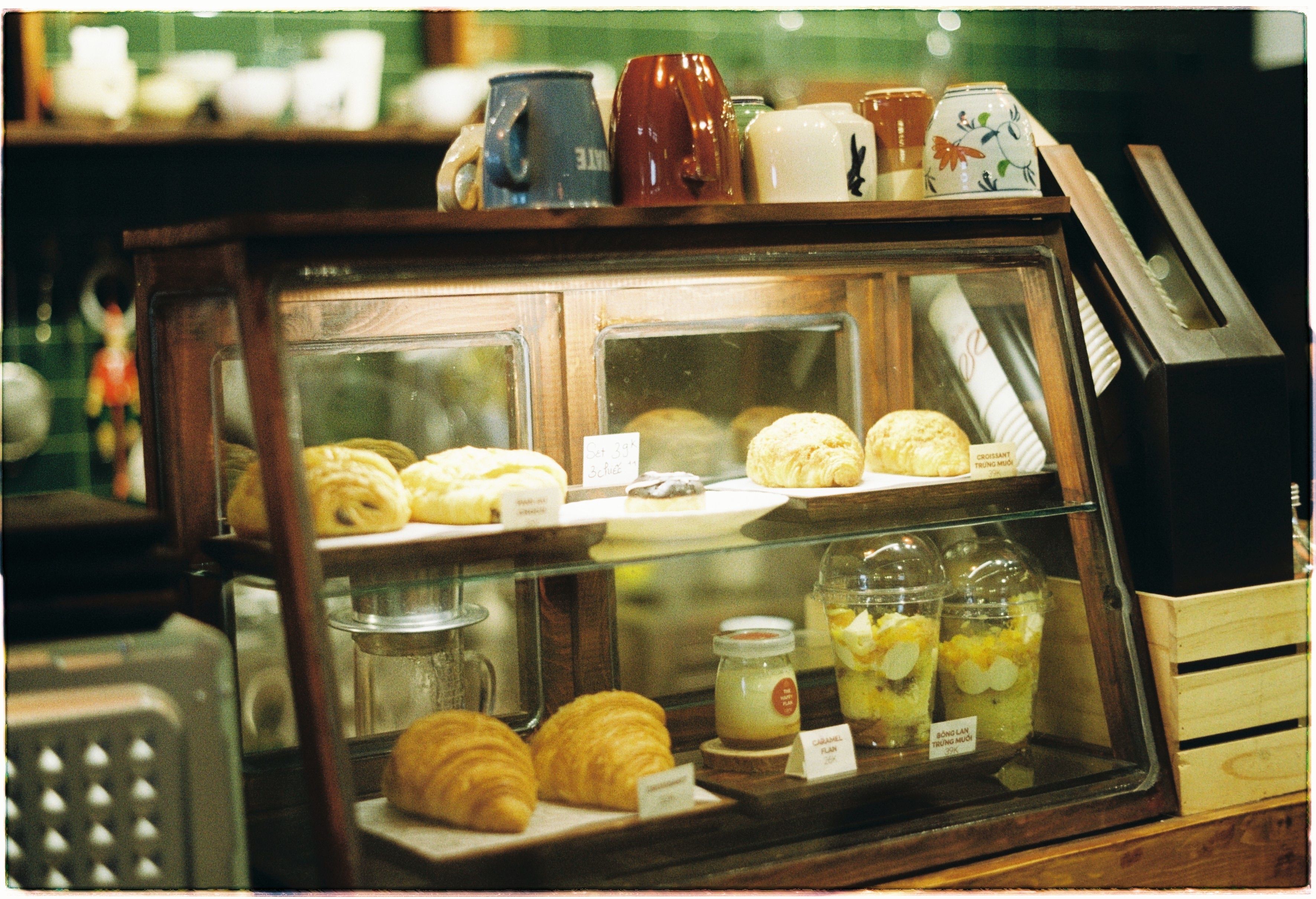 Fresh croissants, pastries, and drinks displayed in a vintage wooden glass display case inside a cafe.