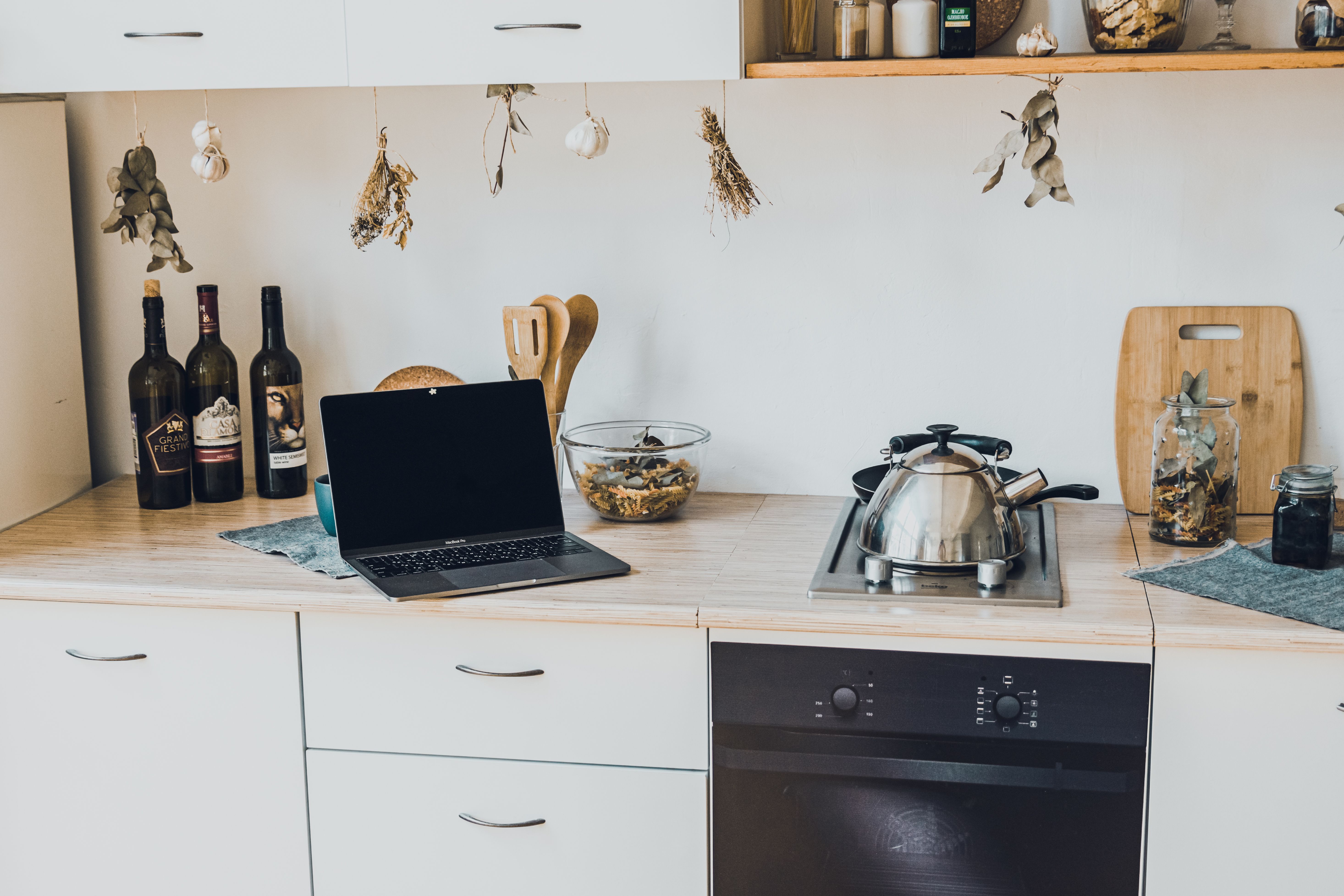An open laptop displaying a black screen sitting on a modern kitchen countertop alongside cooking appliances and wine bottles.