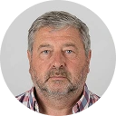 Portrait d'un homme d'âge moyen avec une barbe grise et une chemise à carreaux.