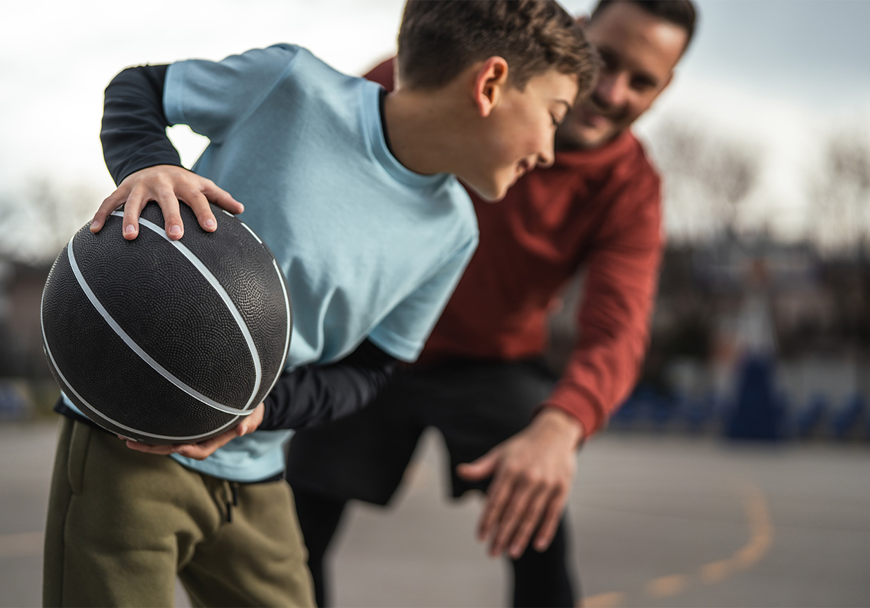 Ein erwachsener Mann und ein Junge spielen zusammen Basketball auf einem Außenplatz