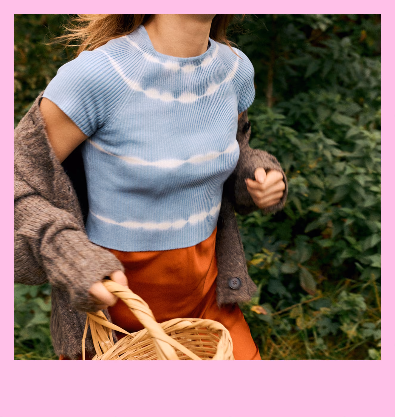 Person wearing blue tie-dye shirt and rust skirt holding a woven basket outdoors.