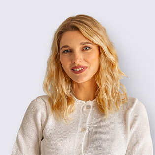 Blonde Frau in weißem Pullover mit sanftem Lächeln vor hellem Hintergrund. Campus-Kurs-Teilnehmerin