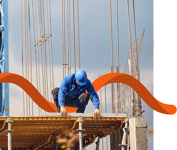 Ouvrier du bâtiment portant un casque et une chemise bleus accroupi sur un échafaudage avec des barres d'armature en arrière-plan.