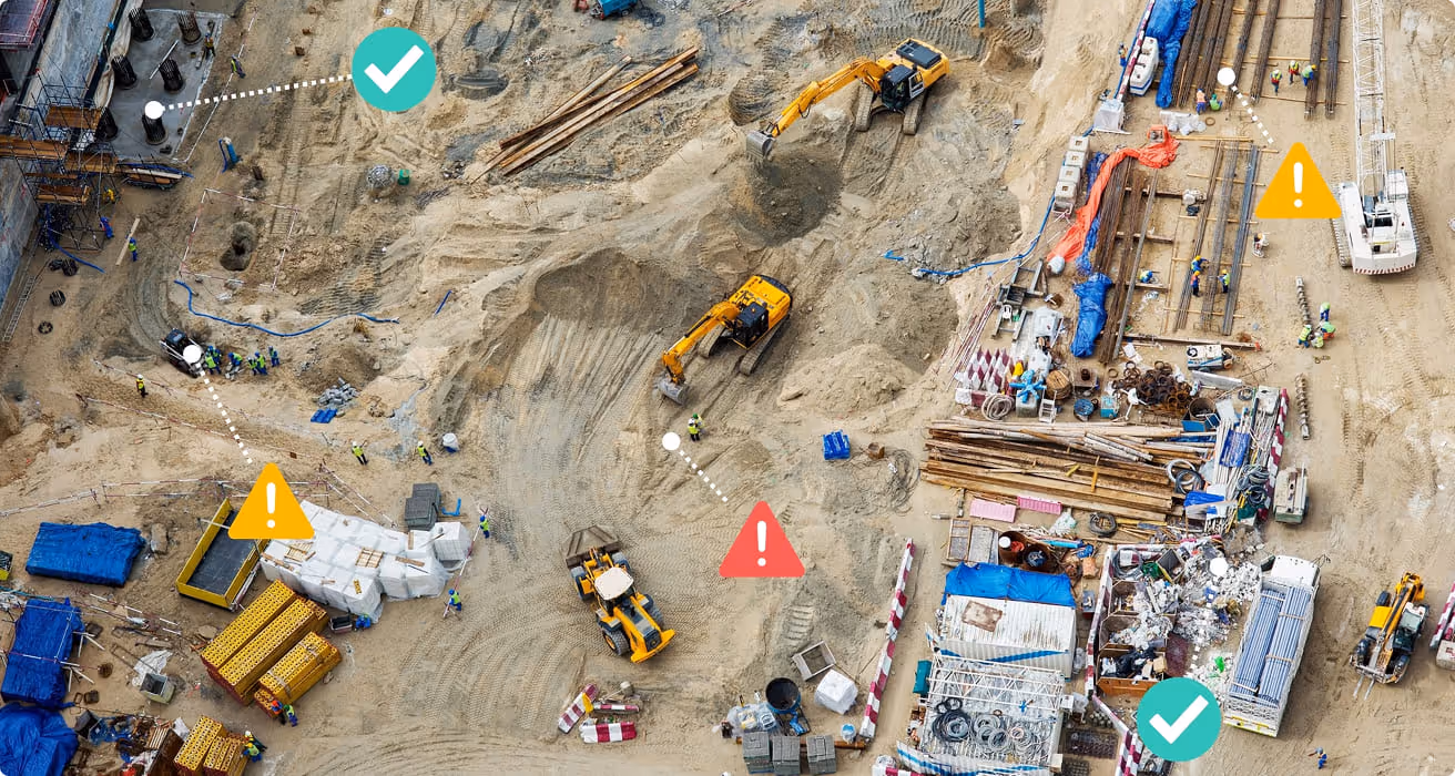 Aerial view of a busy construction site with excavators, workers, building materials, and safety icons indicating check marks and warning alerts.
