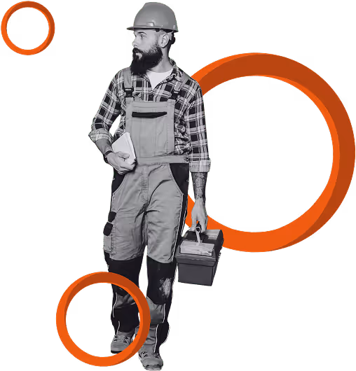 Construction worker in a suit and white hard hat holding a laptop, with blurred workers and scaffolding in the background.