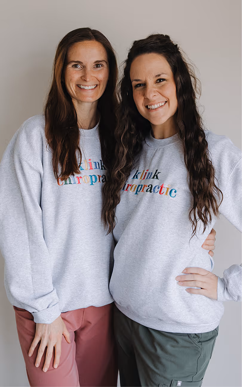 Two women standing next to each other wearing sweatshirts.