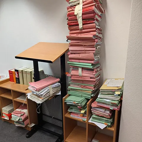 Deckenhoch gestapelter Aktenberg aus farbigen Aktenordnern im Behördenbüro
