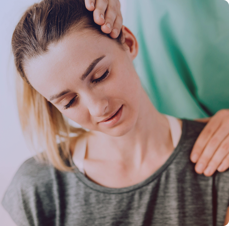 Close-up of a woman with closed eyes receiving a gentle head and shoulder massage from another person wearing a green shirt.