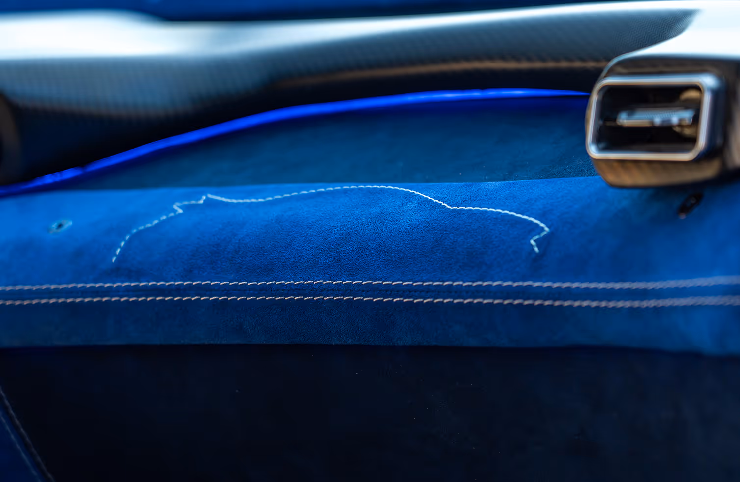 Blue car interior showing illuminated 'QUASAR' logo on metal door sill plate beside blue leather seat controls.