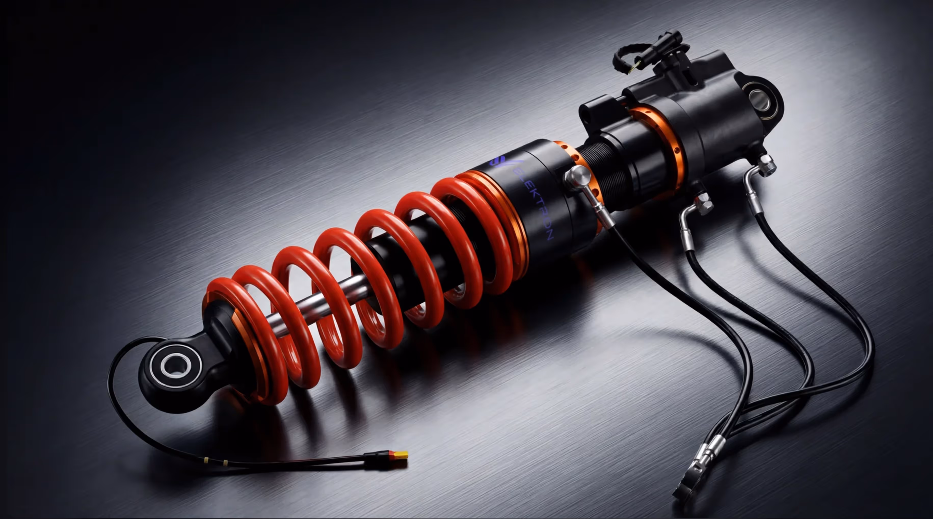 Close-up of a black and red coil shock absorber with attached hydraulic hoses on a metallic surface.