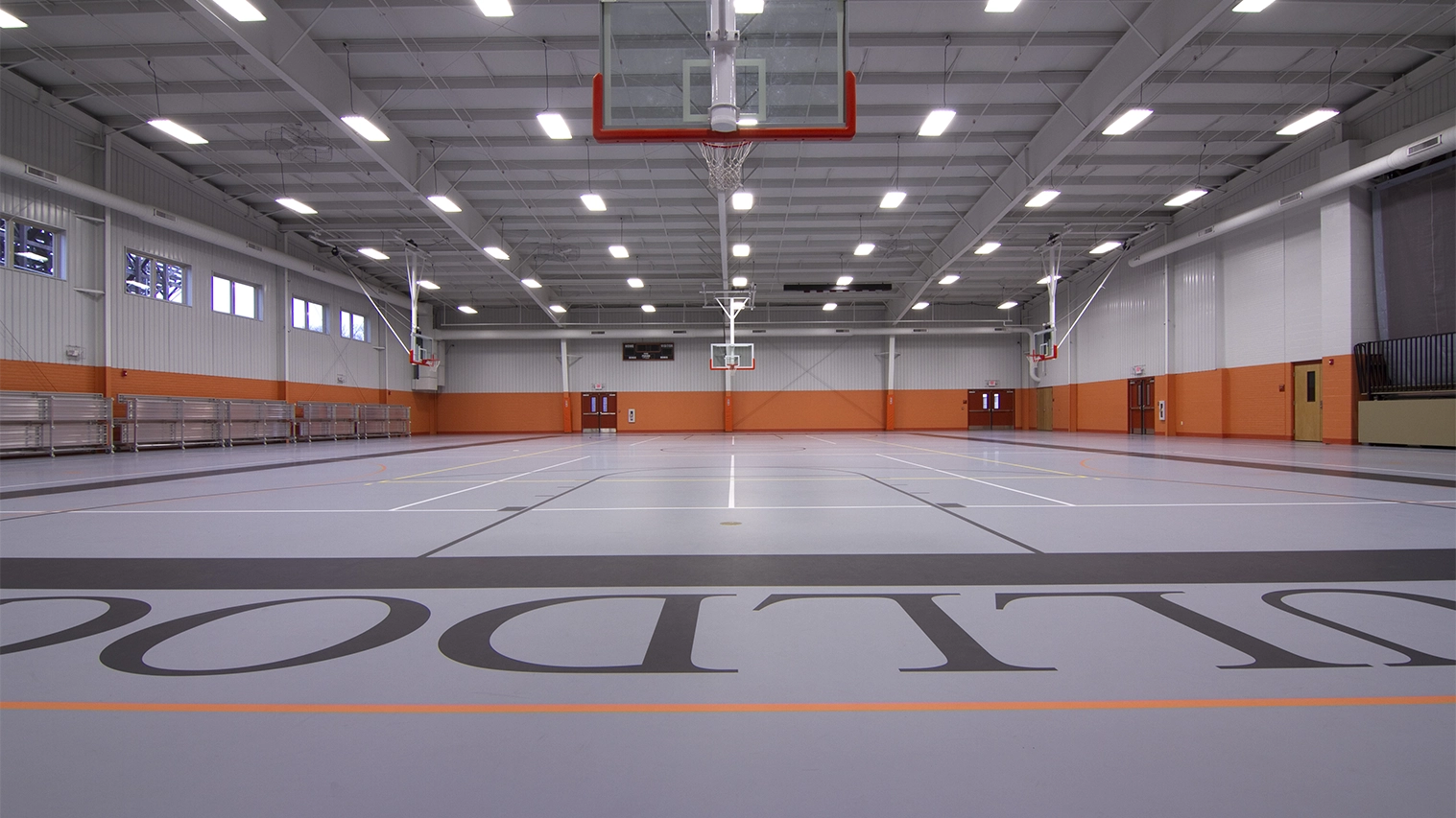 Empty indoor basketball court with polished floor, orange and white walls, and multiple basketball hoops.