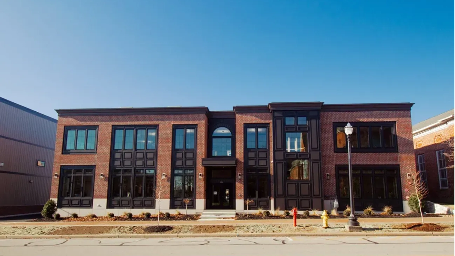 Two-story commercial building with brick facade, black window frames, and a central entrance under a clear blue sky.
