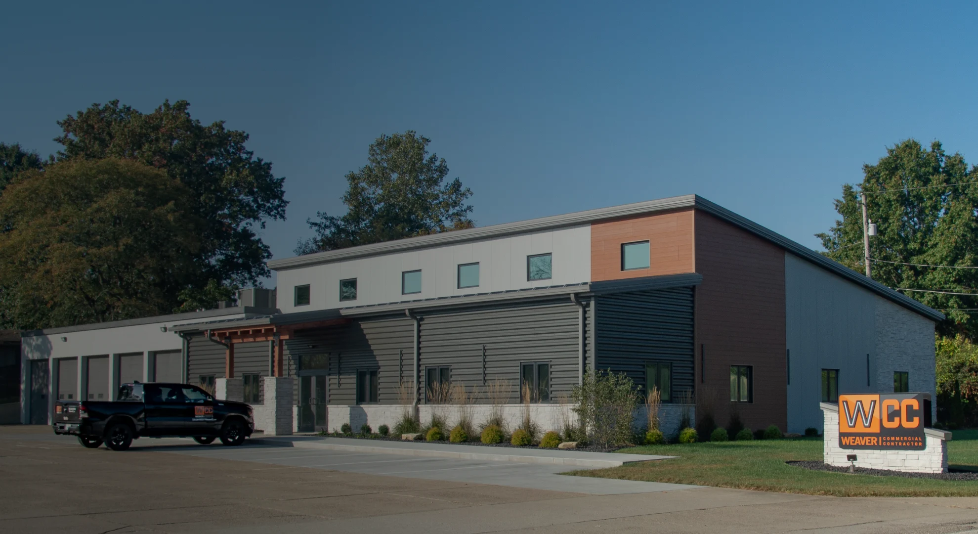 Modern building with beige and brick exterior, large glass windows, and a green lawn in front.