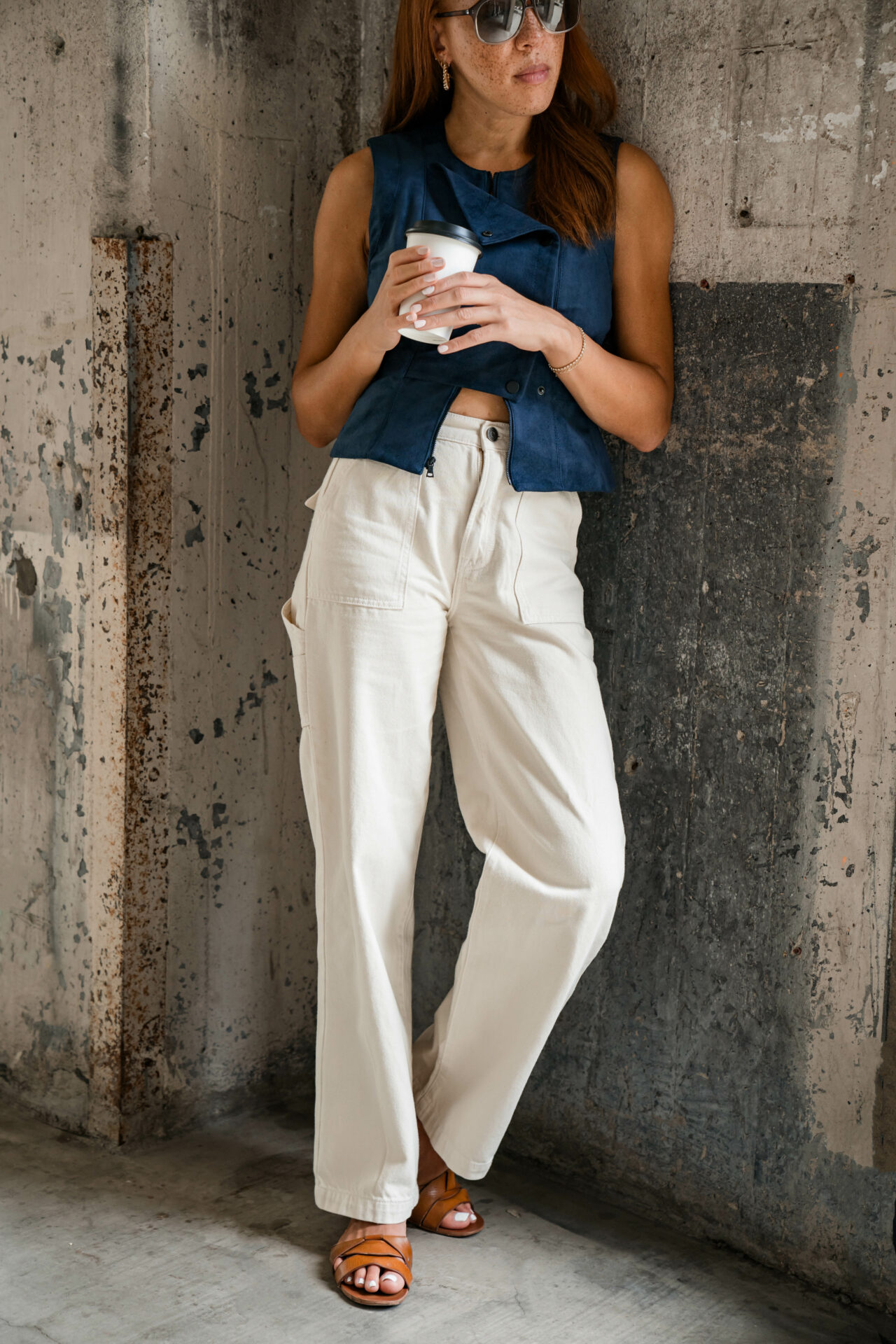 woman standing next to a wall holding a drink