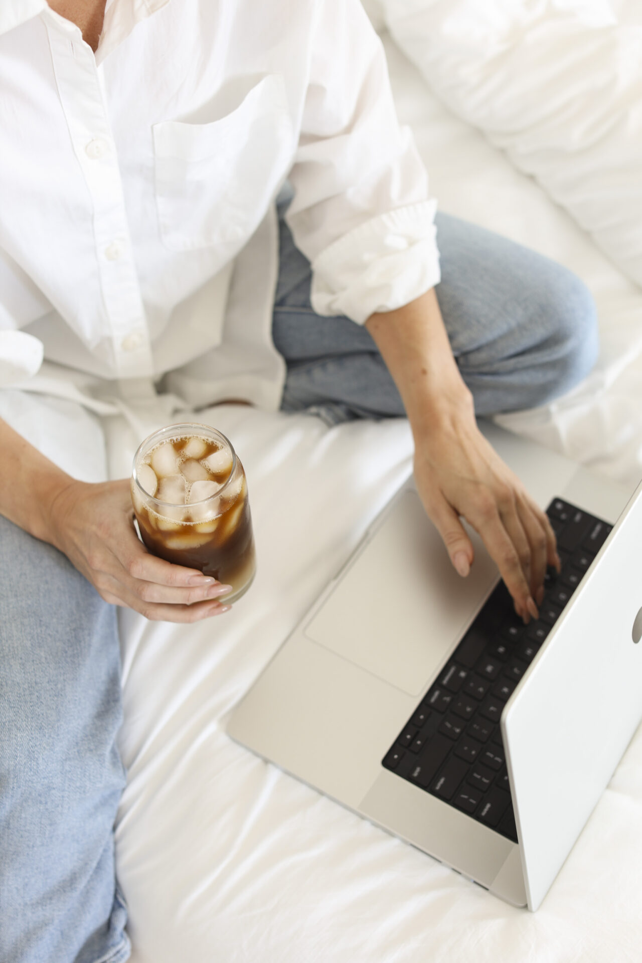 woman typing on a laptop while holding a drink in another hand