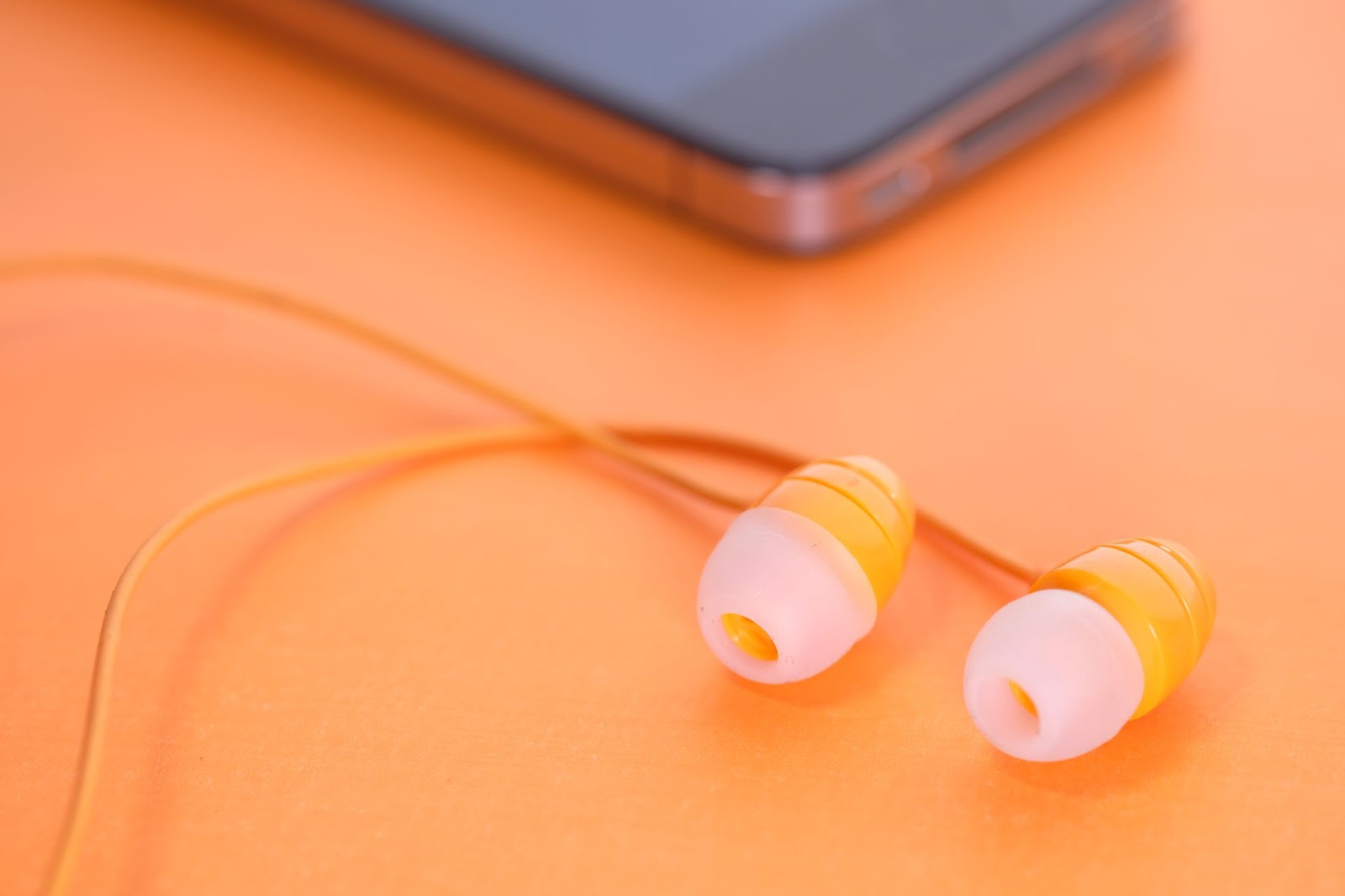 A pair of earbuds next to a smartphone on an orange background.