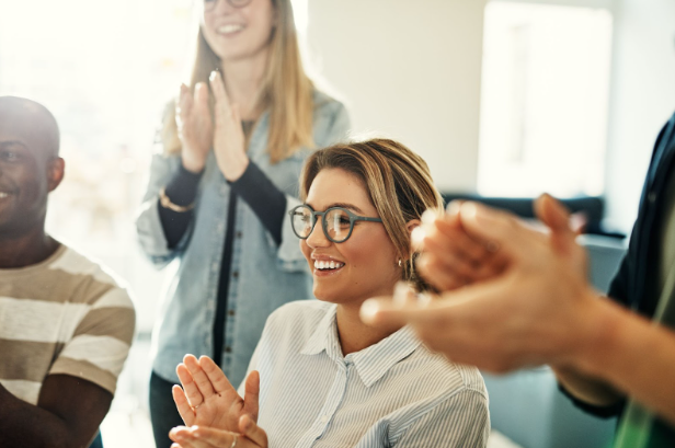 Diverse employees smiling and clapping during an office meeting.
