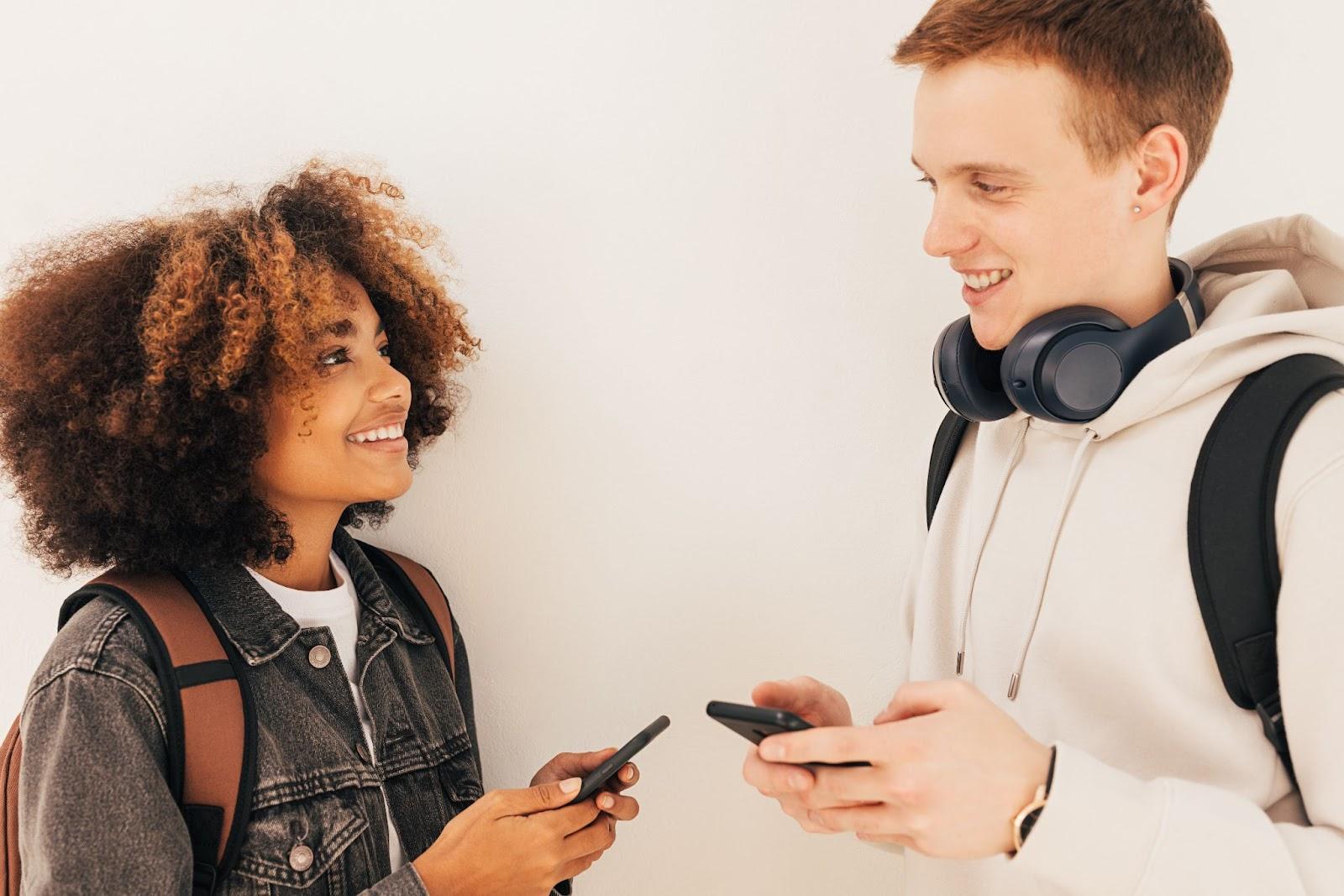 A young female and male looking at each other, holding smartphones.