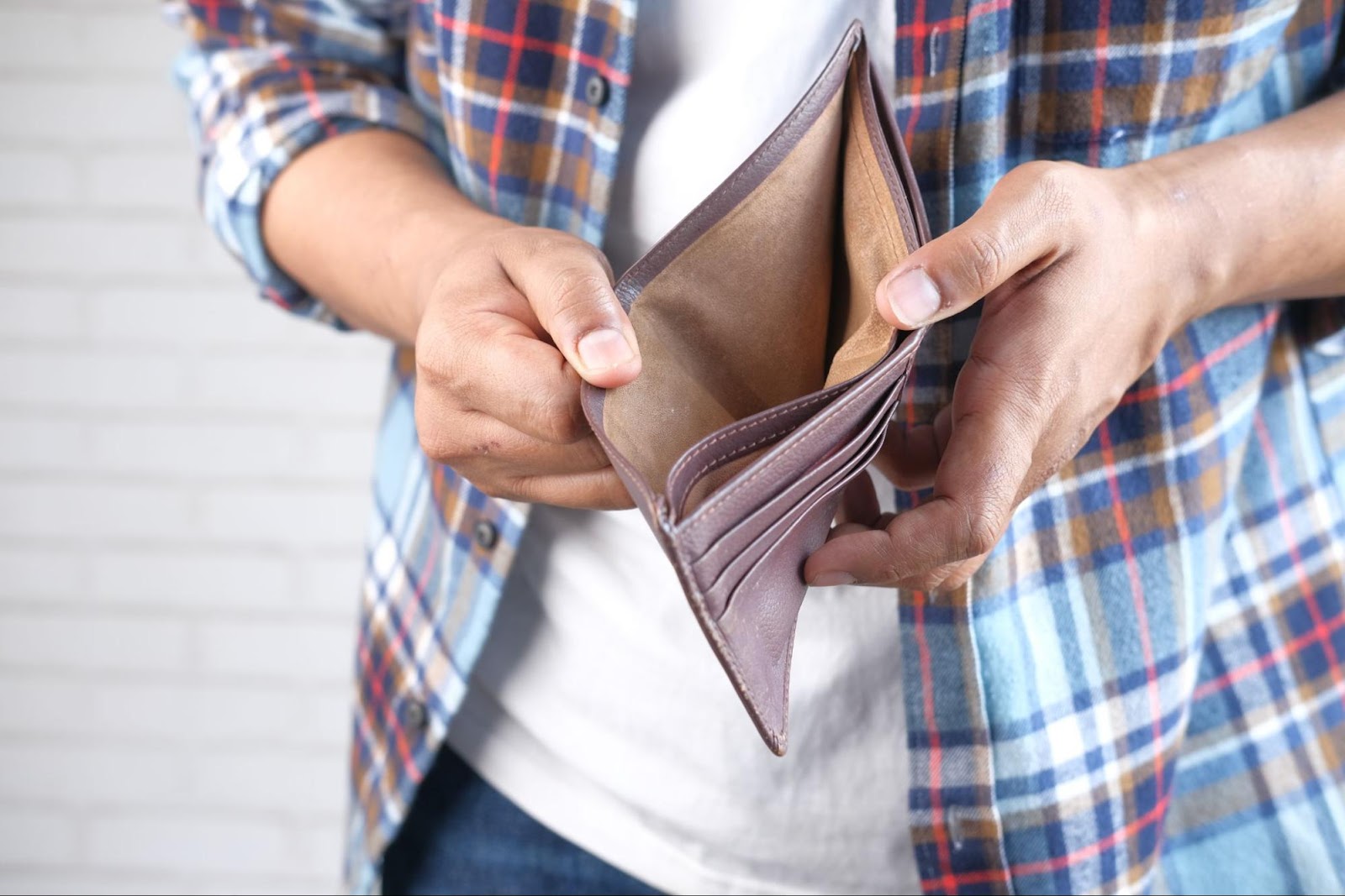 A man in a plaid shirt holding an empty wallet.