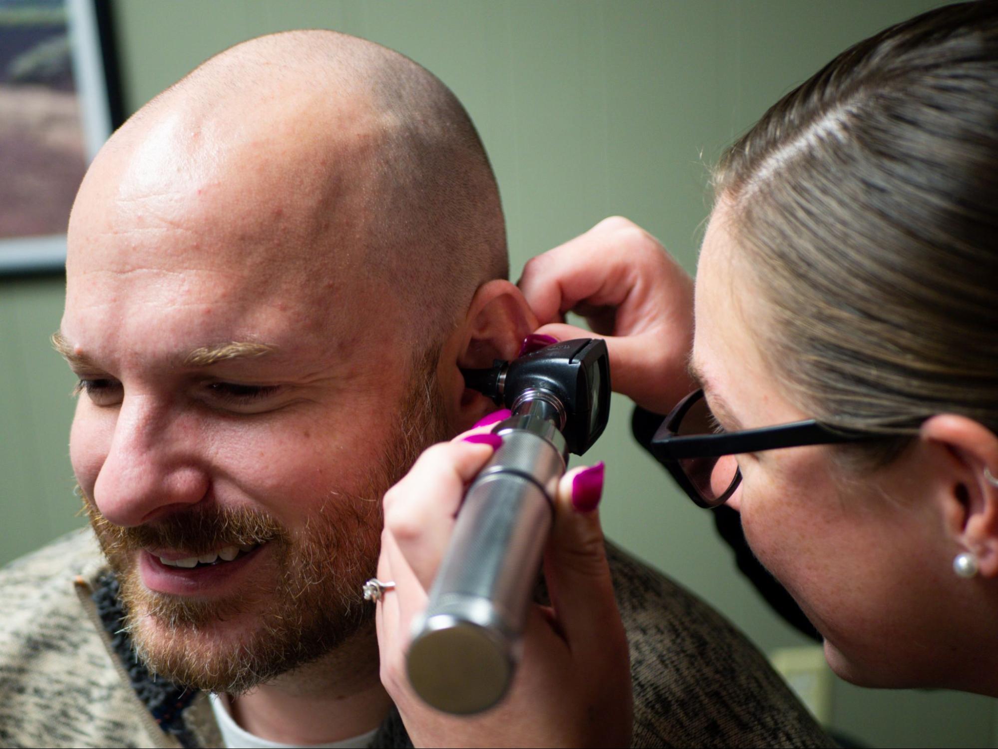 Audiologist examines a man's ear using a handheld instrument.