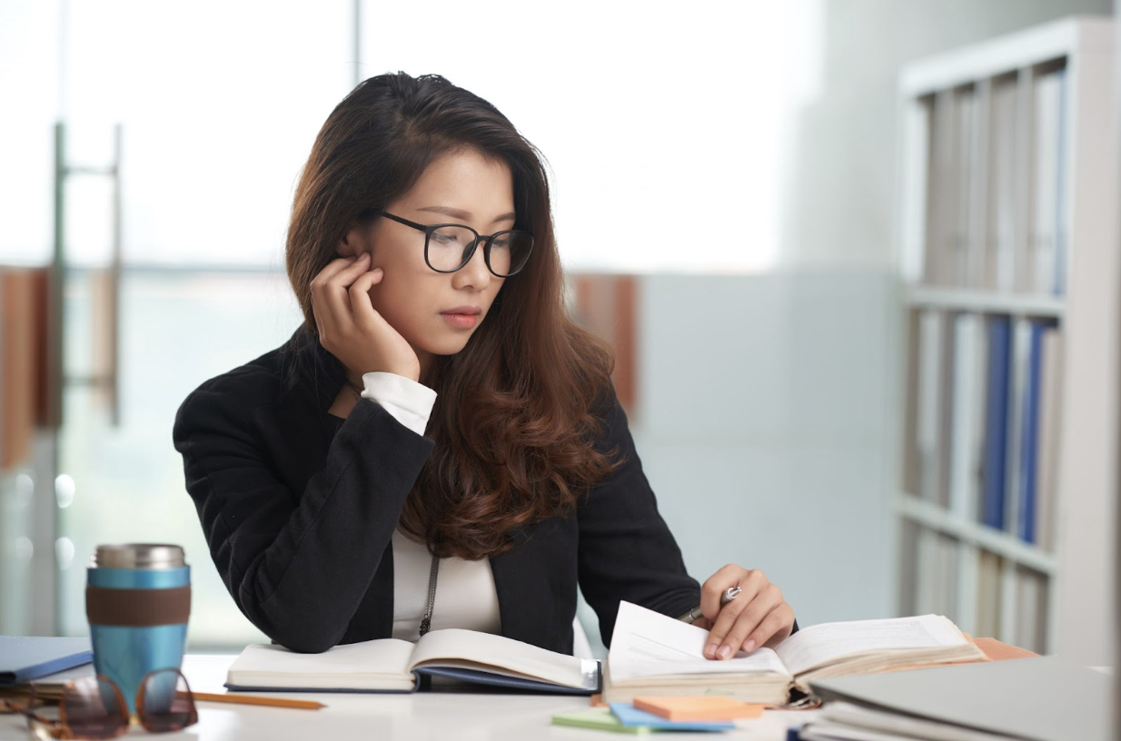 Young female wearing eyeglasses and business attire. She is reading and taking notes. Photo by DragonImages.