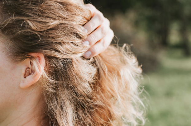 Side view of woman holding her hair back to show a small hearing aid in her left ear.