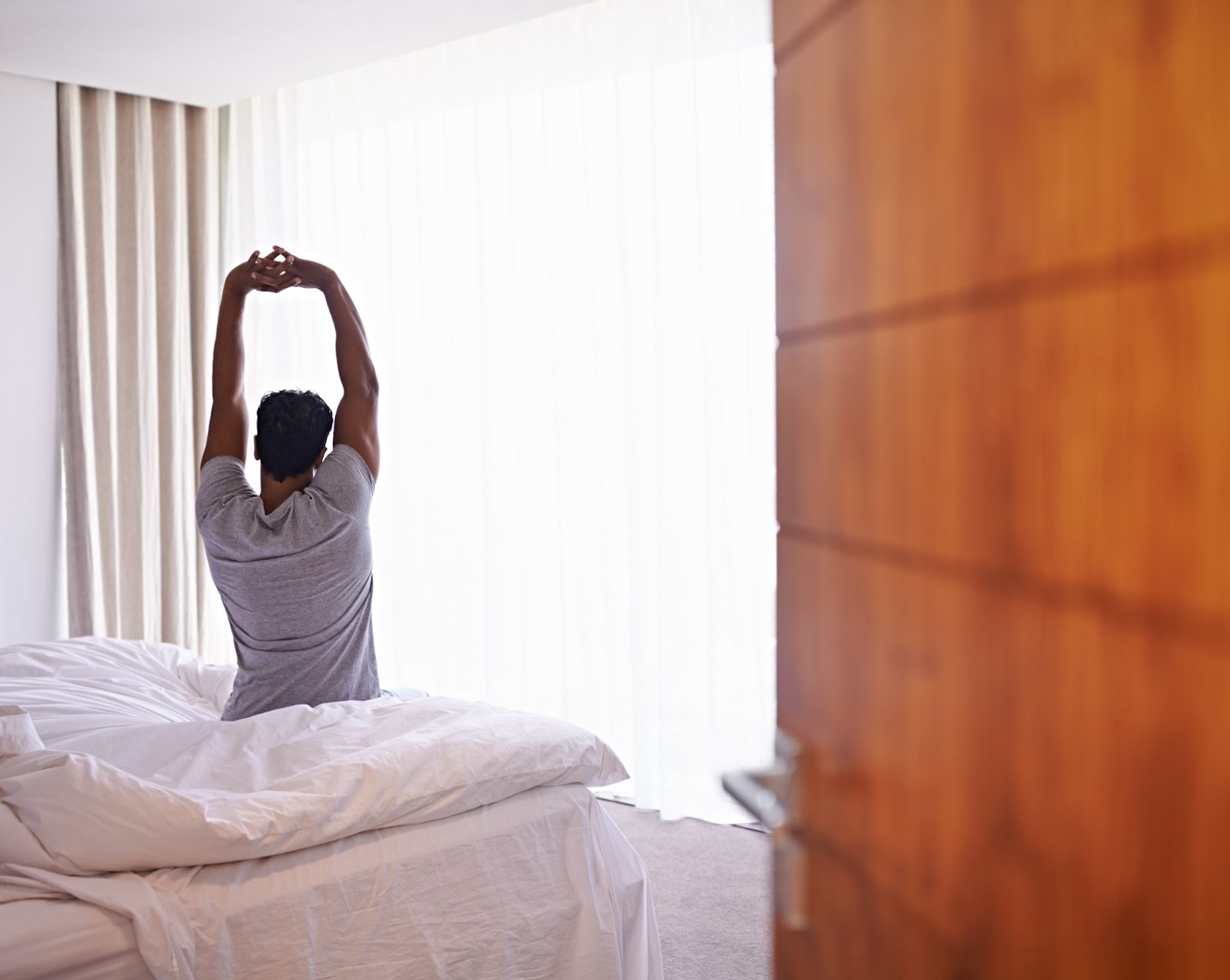 A person stretches while sitting on a hotel bed.