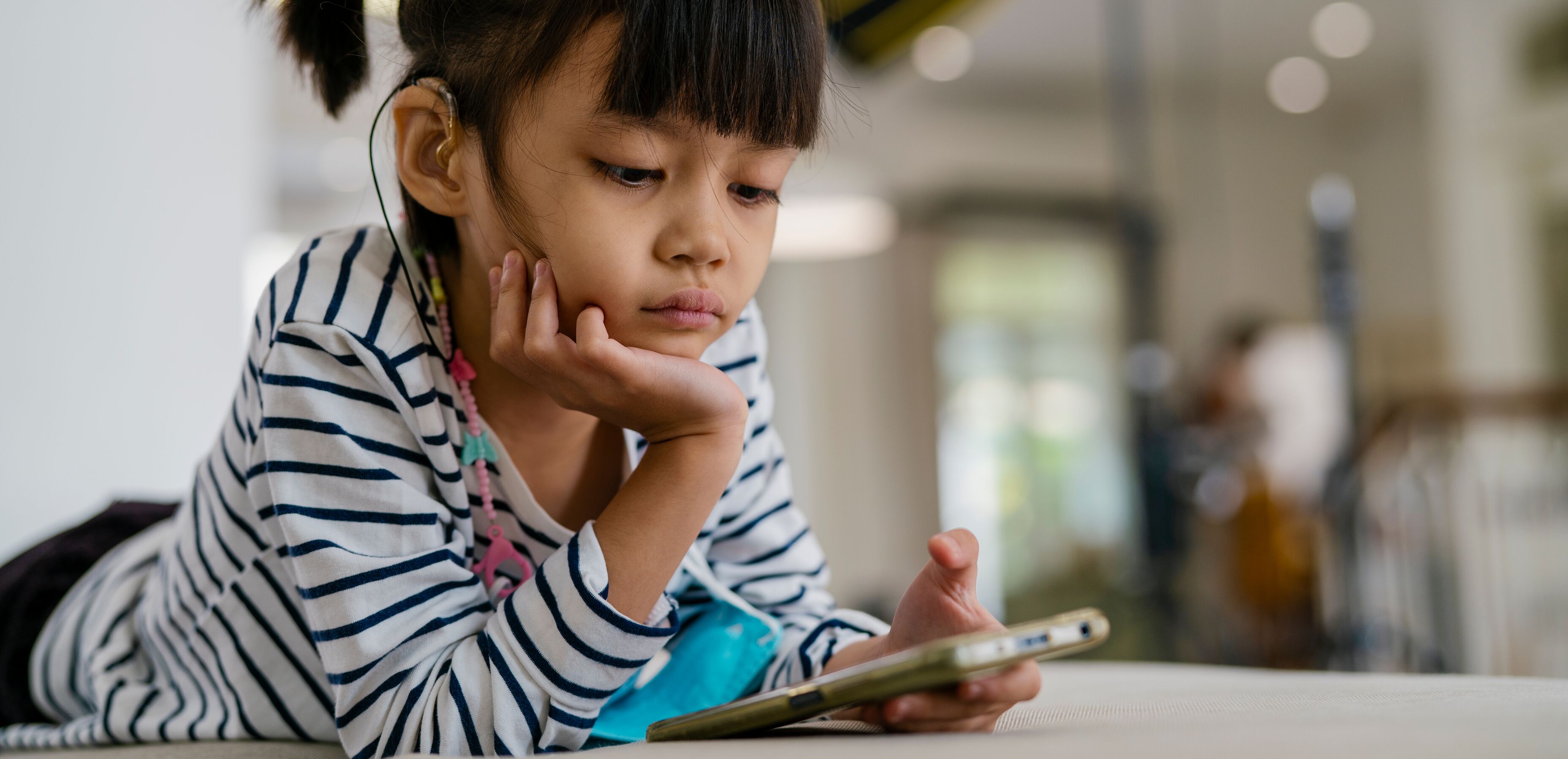 Girl wearing a hearing aid and playing a smartphone.