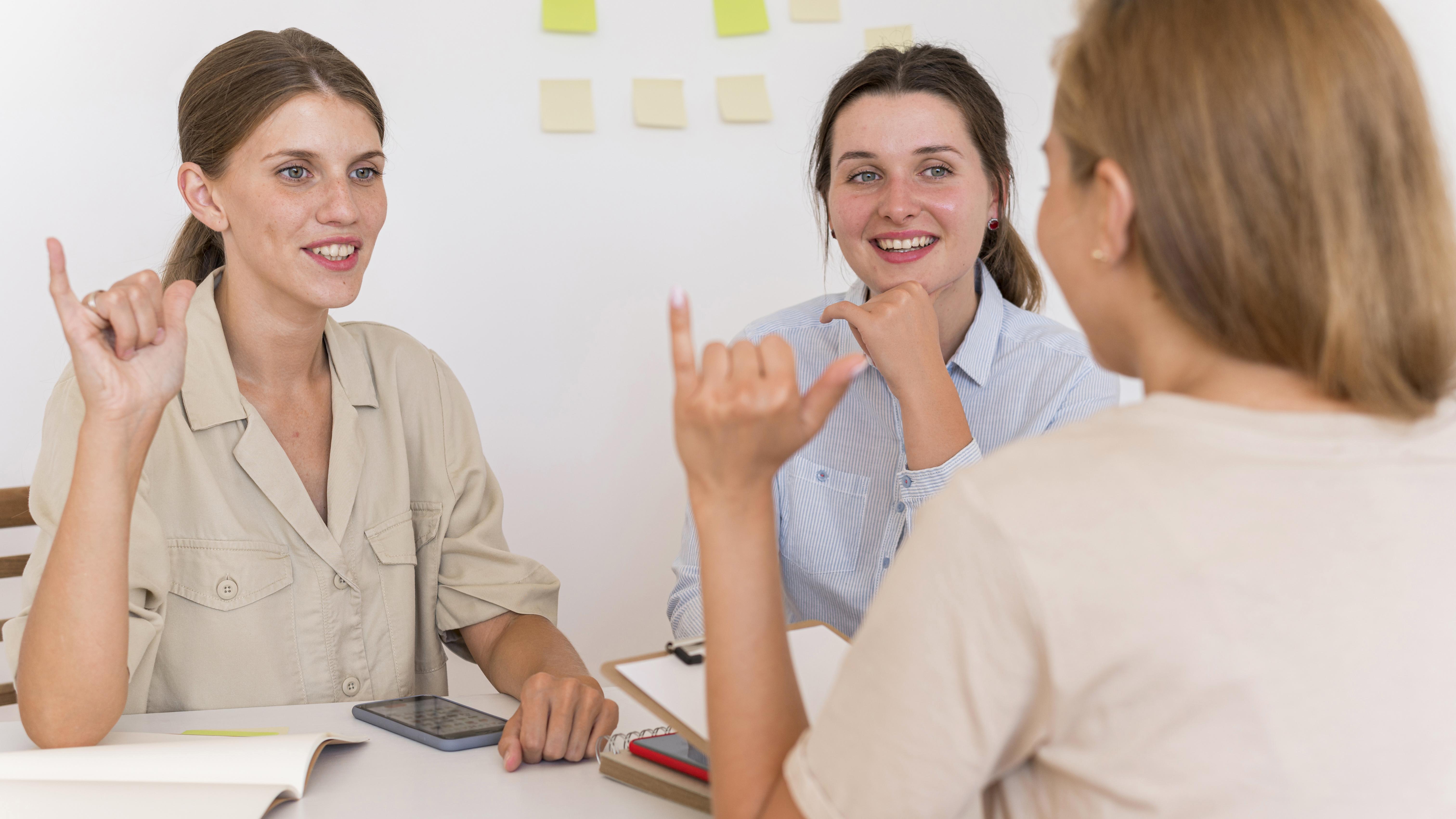 smiley women conversing table using sign language