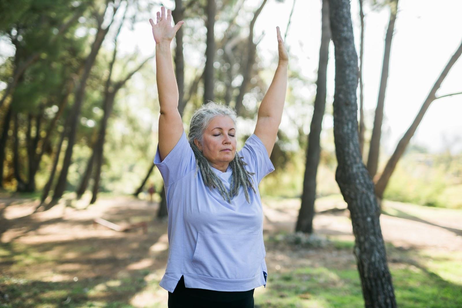 A mature woman outdoors stretching her arms with eyes closed