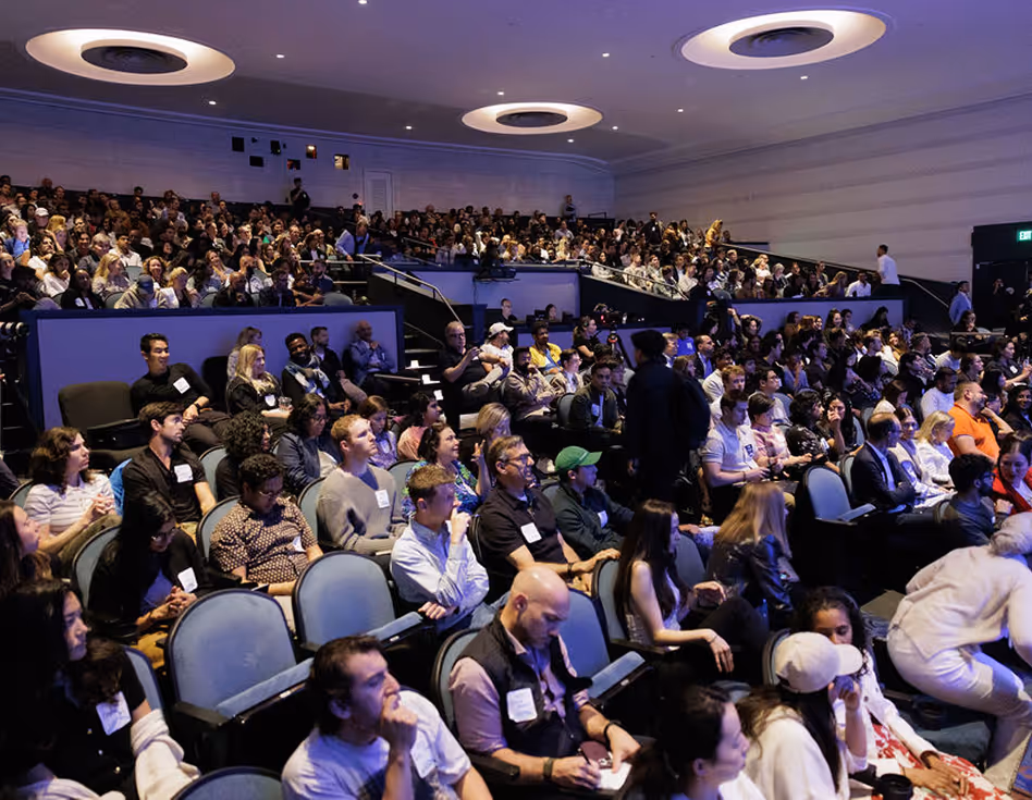 Large audience seated in a tiered auditorium attentively watching a presentation or event.